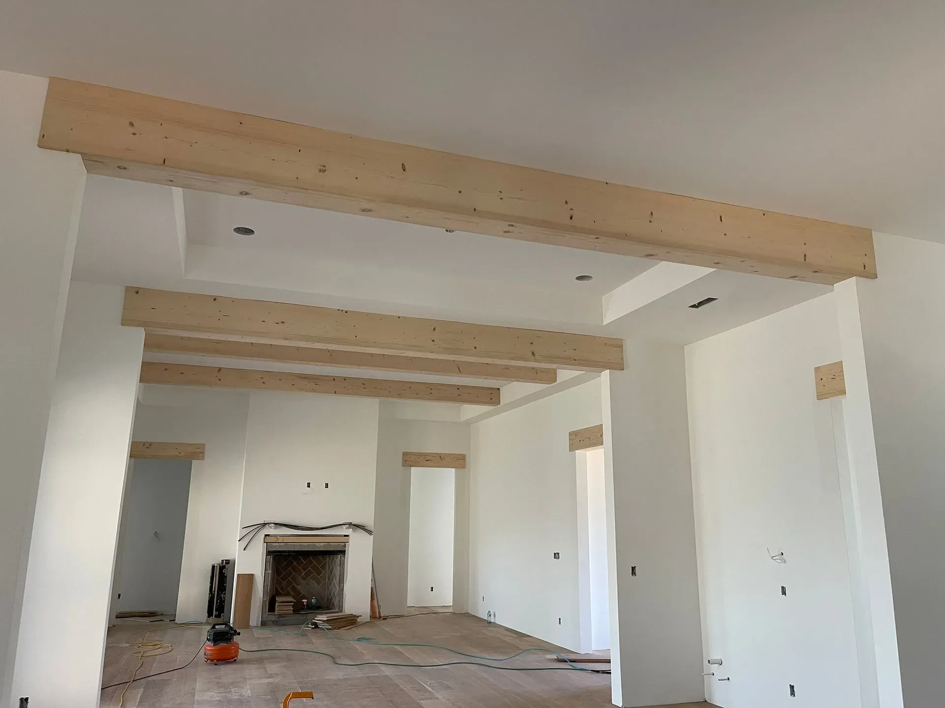Empty unfinished living room with exposed wooden beams and a fireplace under construction