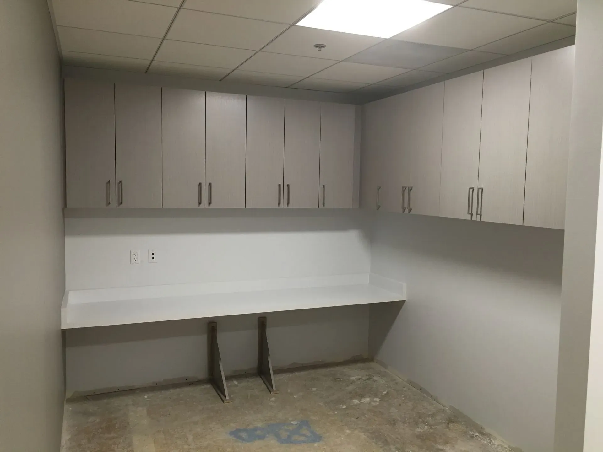 Empty office storage room with gray cabinets, white countertop, and a worn floor.