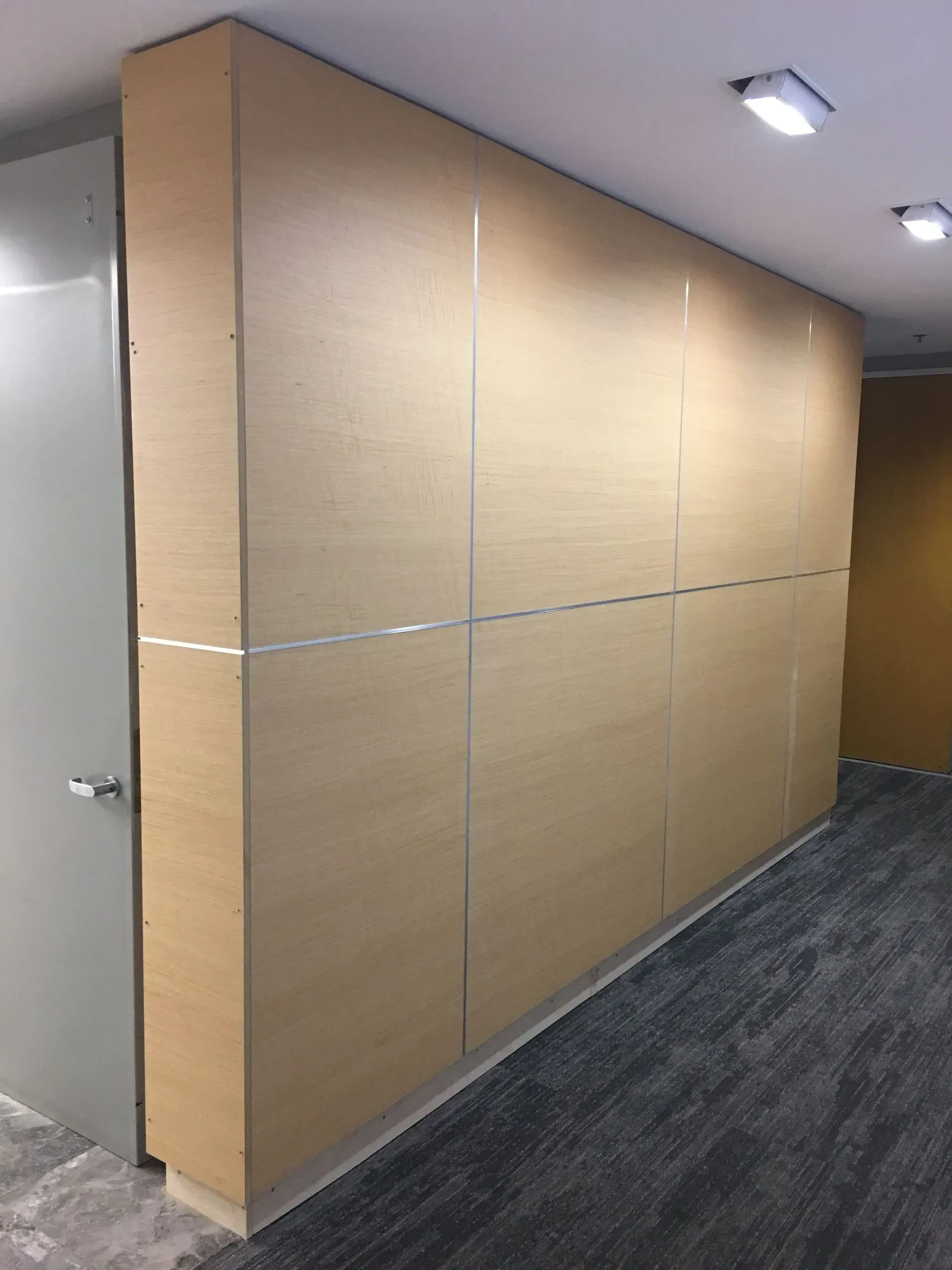 Large beige temporary wall panel in an office hallway with recessed ceiling lights and gray carpet.