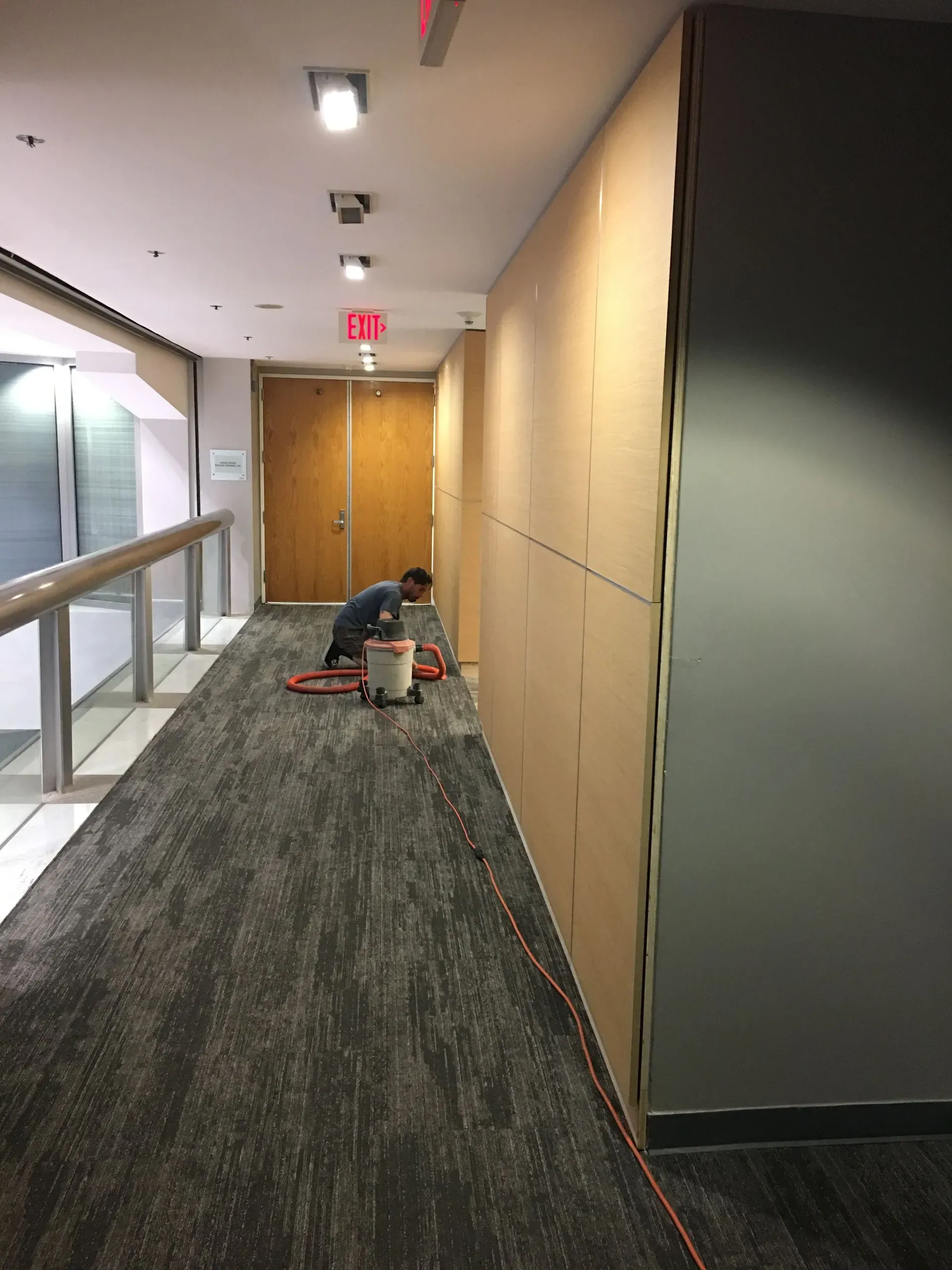 Person cleaning a carpeted hallway beside a glass railing and wooden wall panels