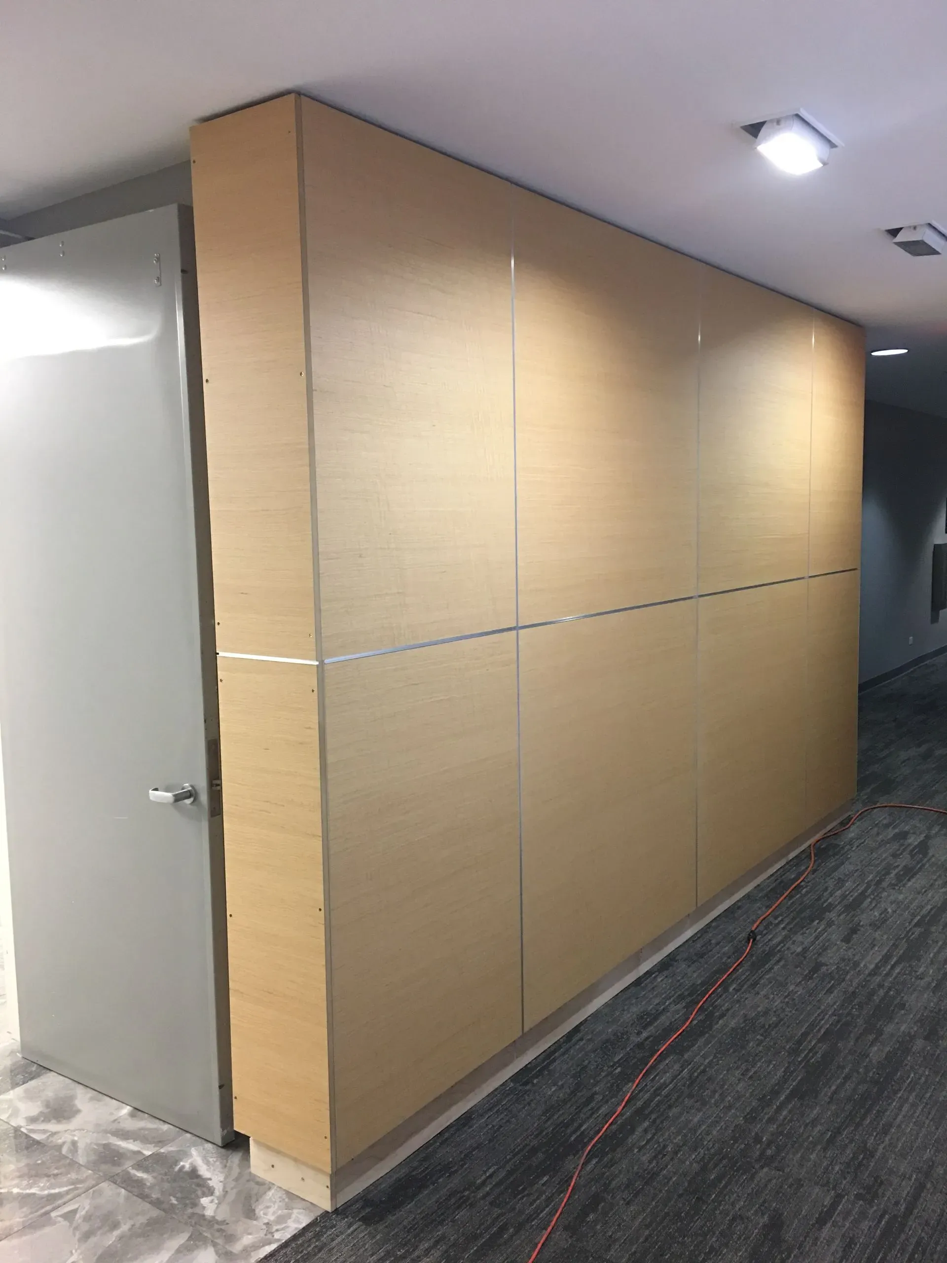 Hallway with a long beige wall panel and gray carpet under ceiling lights