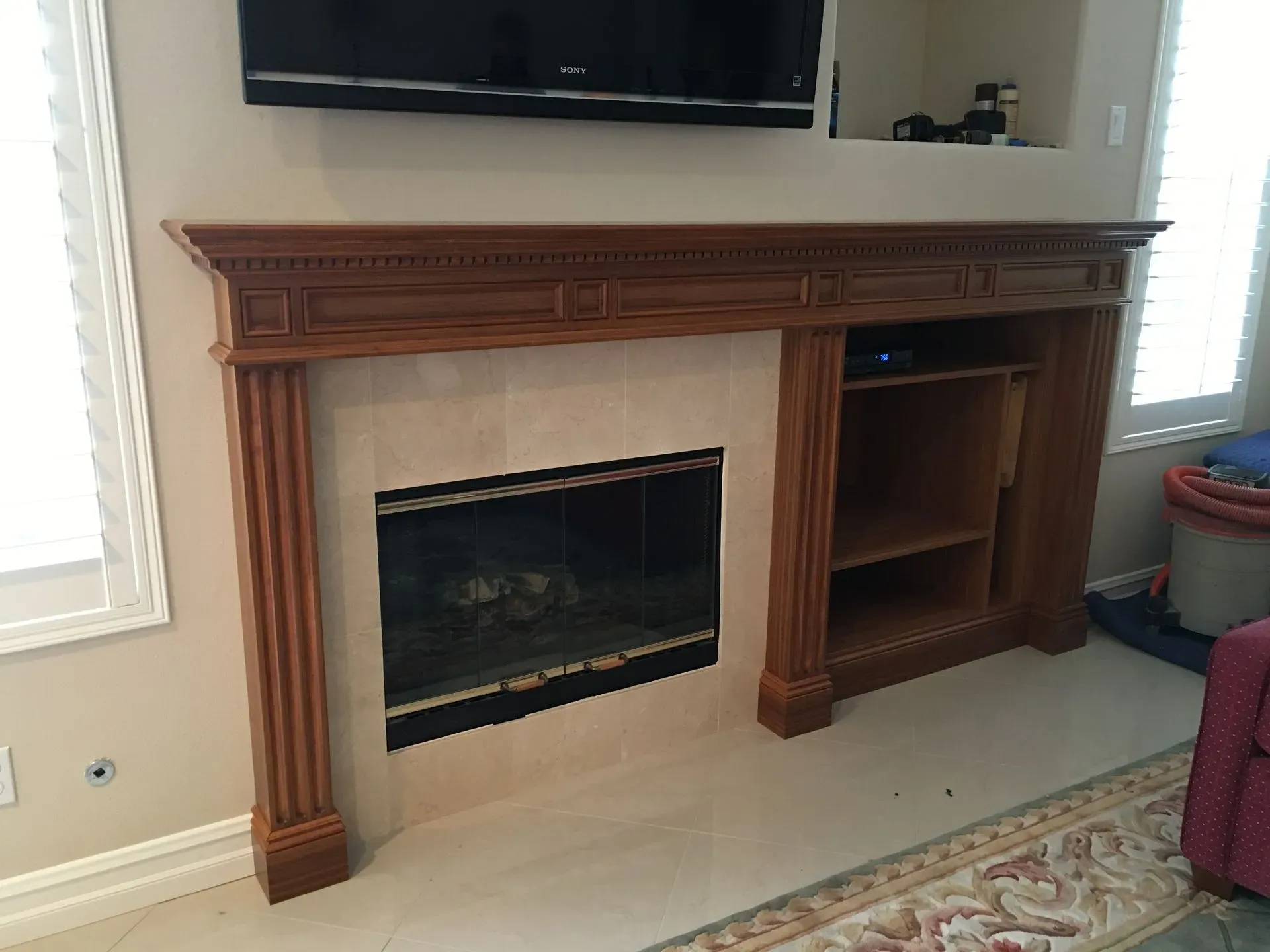 Wooden fireplace mantel with built-in TV above, fireplace opening, and shelves in a bright living room