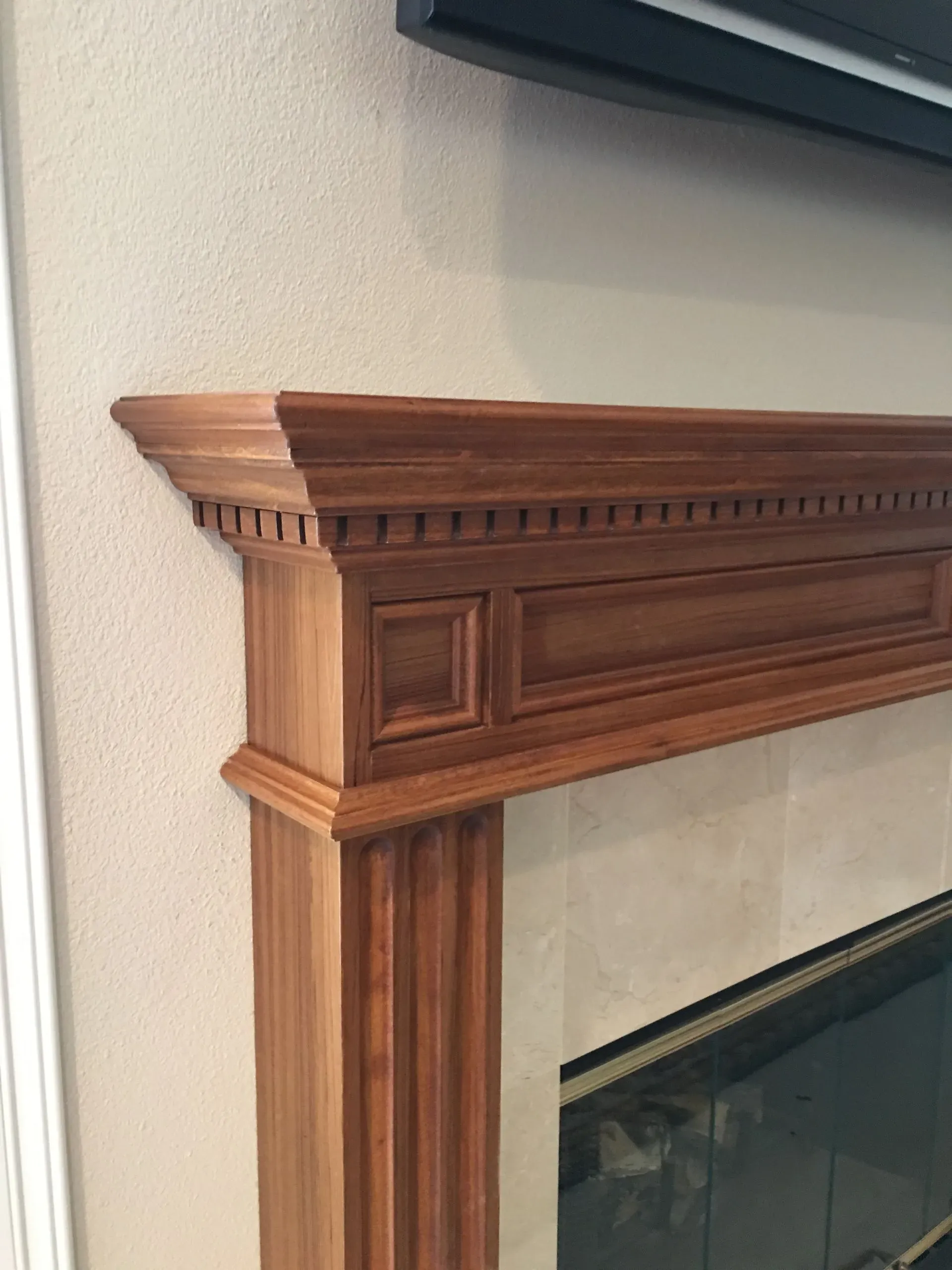 Close-up of a wooden fireplace mantel with decorative trim beside a wall-mounted TV