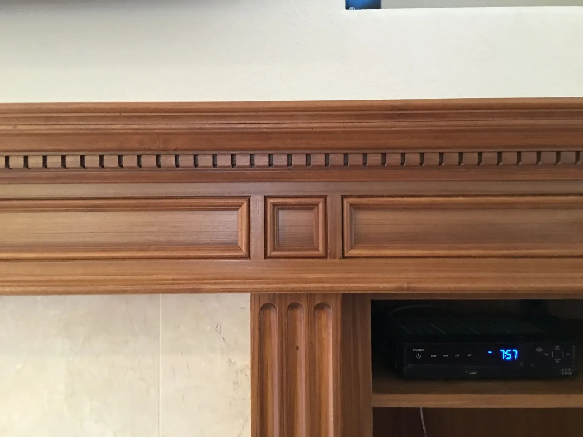 Wooden fireplace mantel with decorative trim and a black electronic device inset on the right