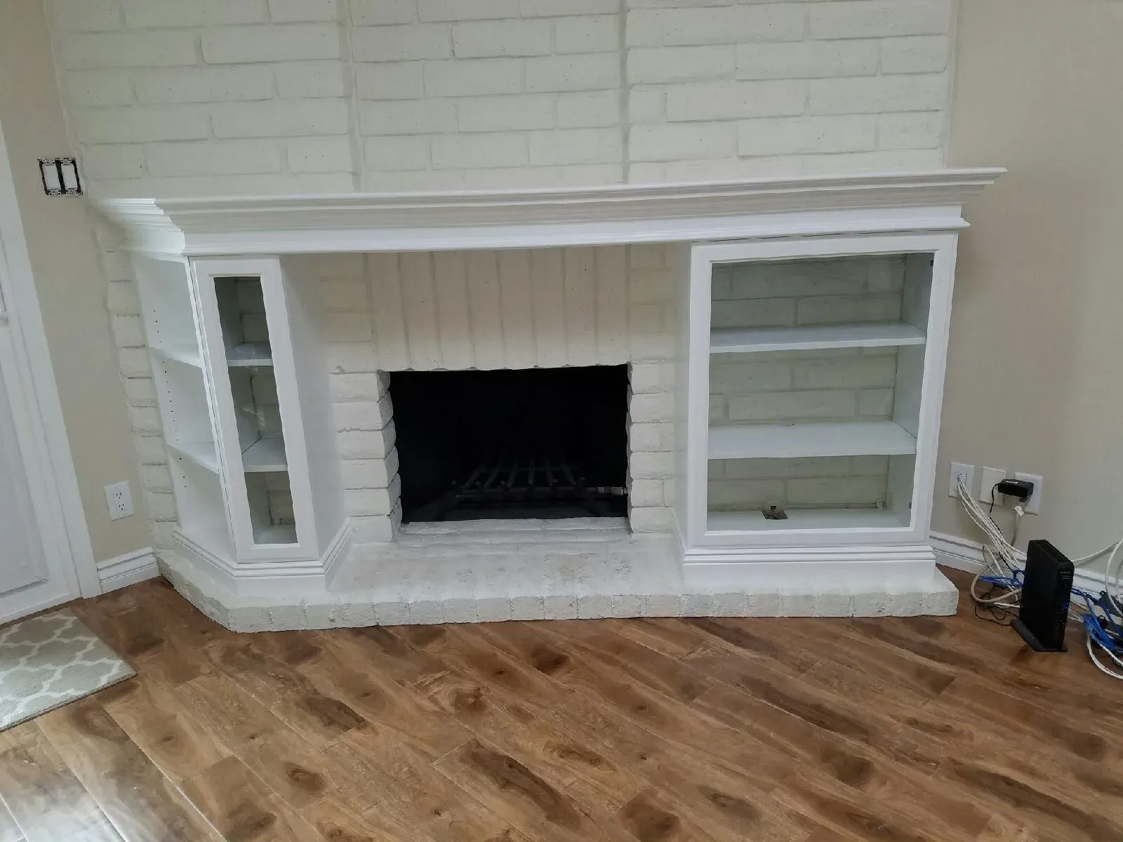 White brick fireplace with mantel and glass-front cabinets in a room with wood floors and beige walls