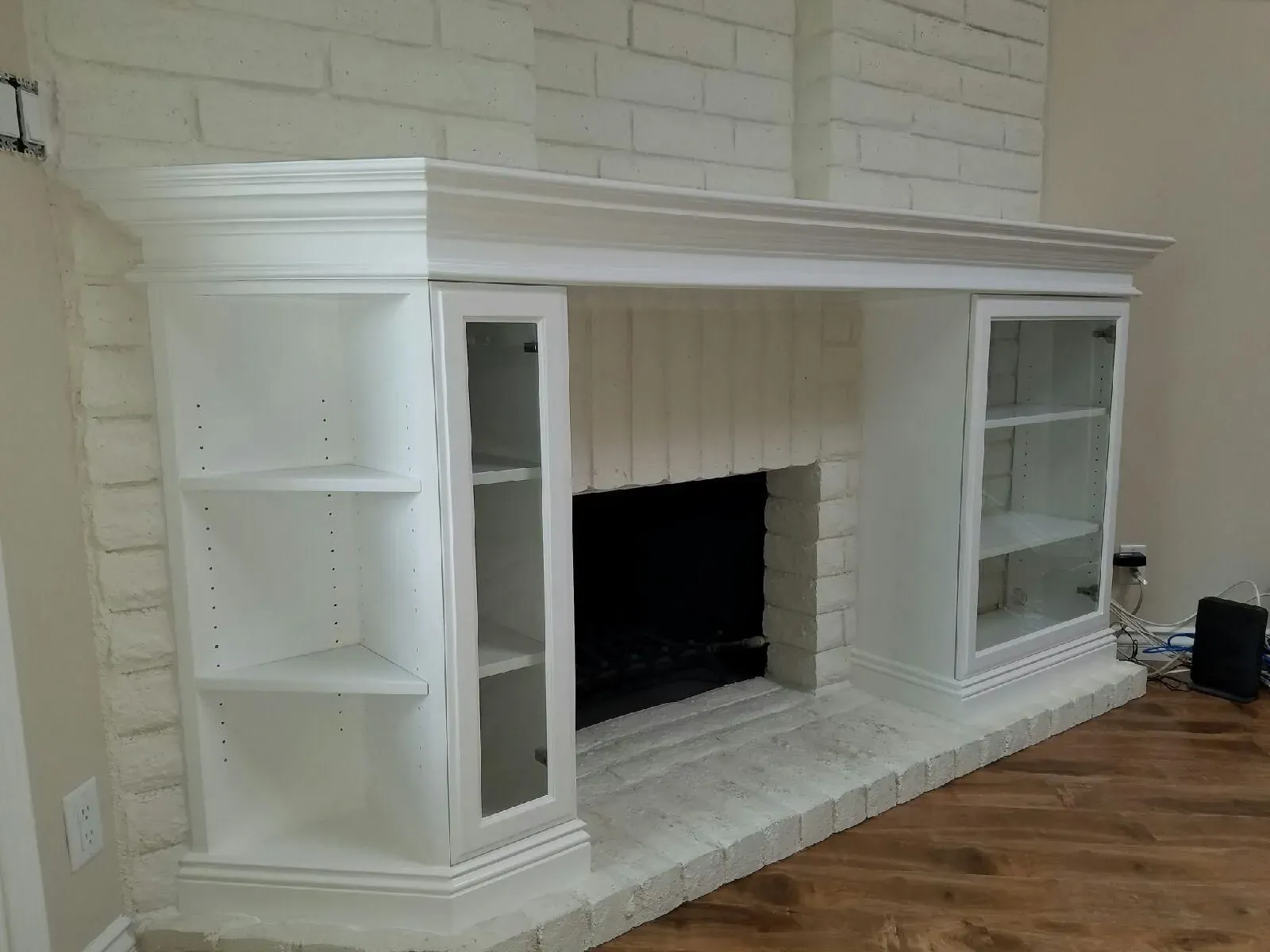 White built-in fireplace mantel with shelves against a brick wall and hardwood floor
