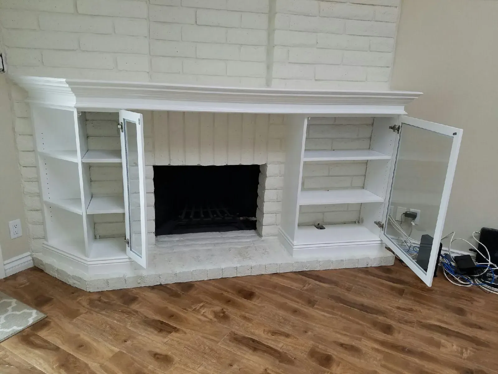 White built-in fireplace with open shelves and cabinet doors against a brick wall, on a hardwood floor