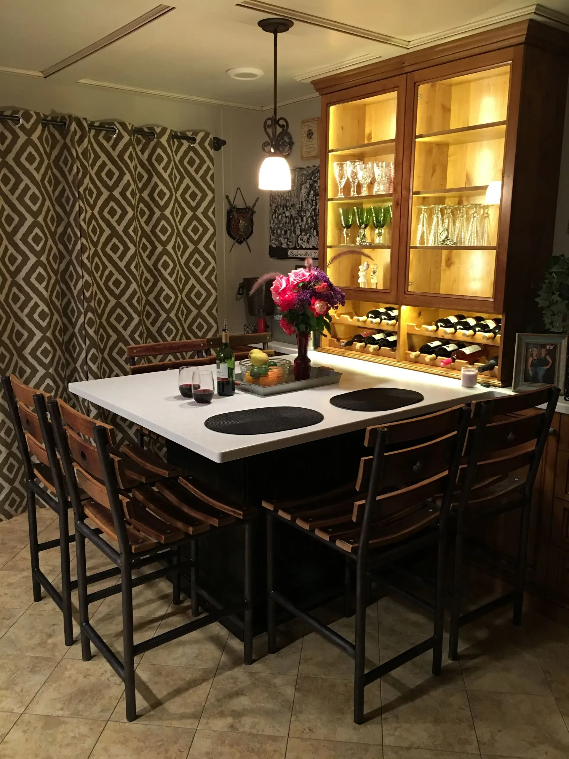Dining area with a wooden table, black chairs, pendant light, and illuminated glass cabinet against patterned walls.