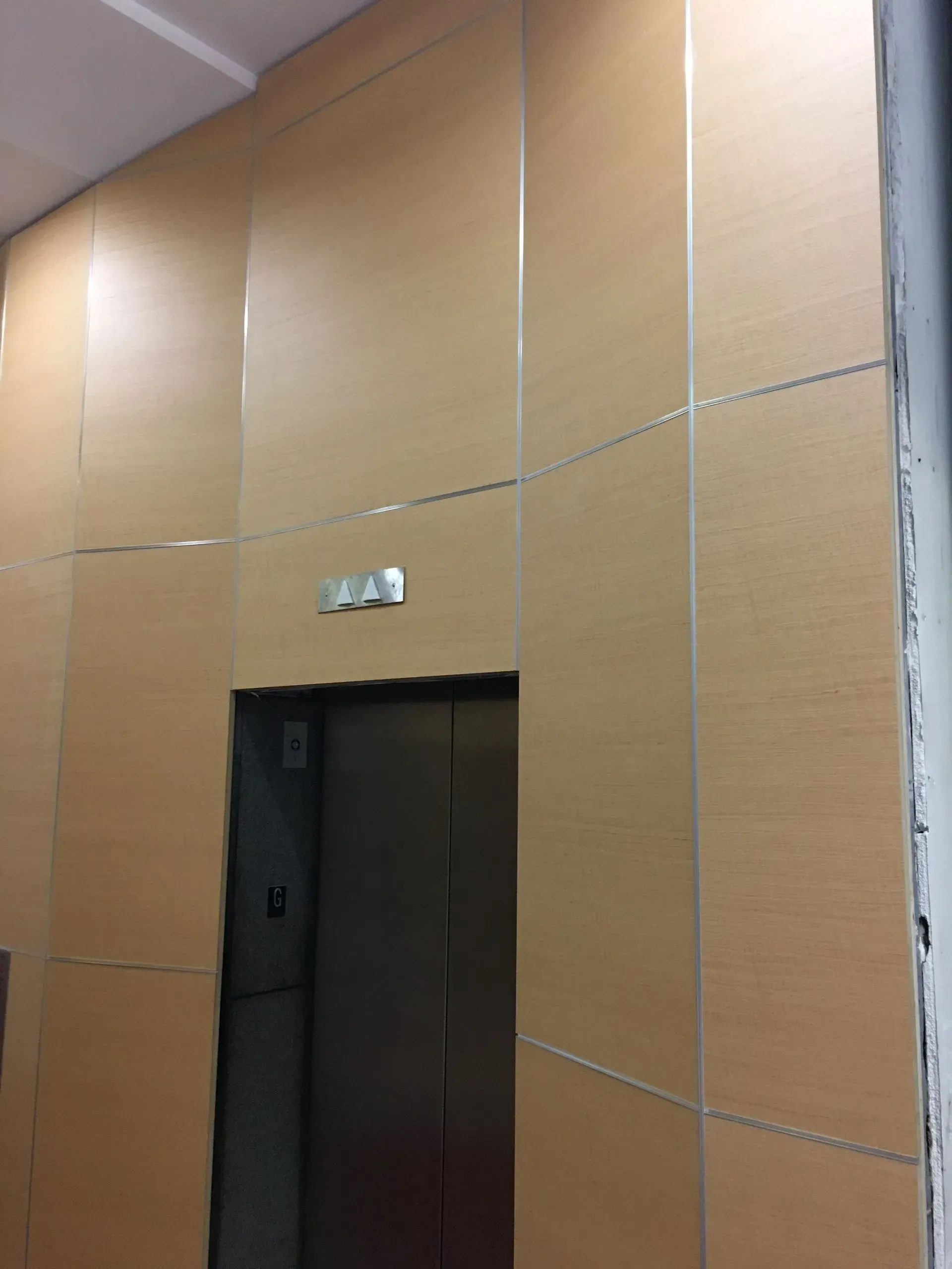 Empty elevator entrance with beige wall panels and a small sign above the doorway.
