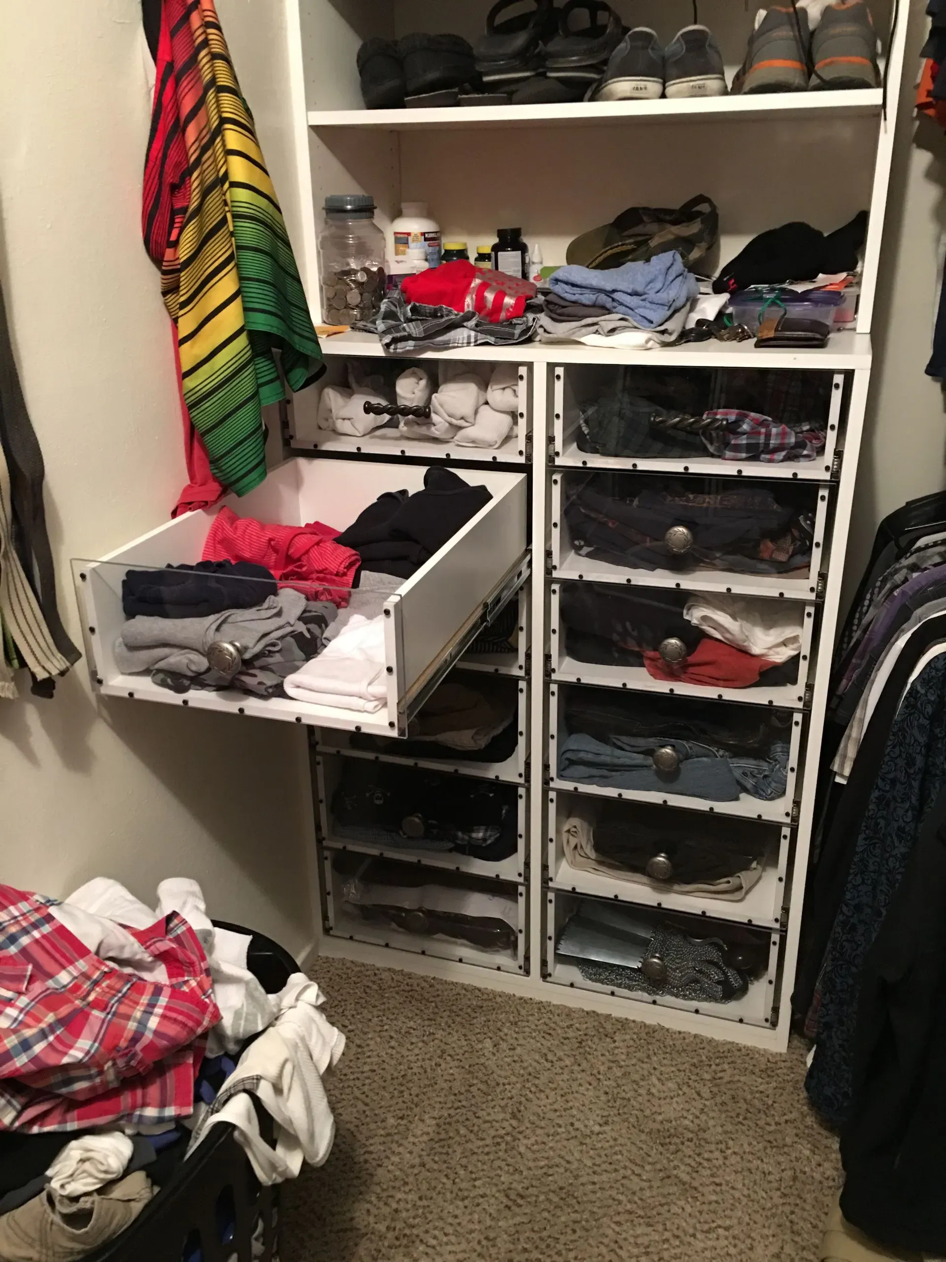 Open closet with shelves and drawers full of folded clothes, shoes, and a colorful hanging garment.