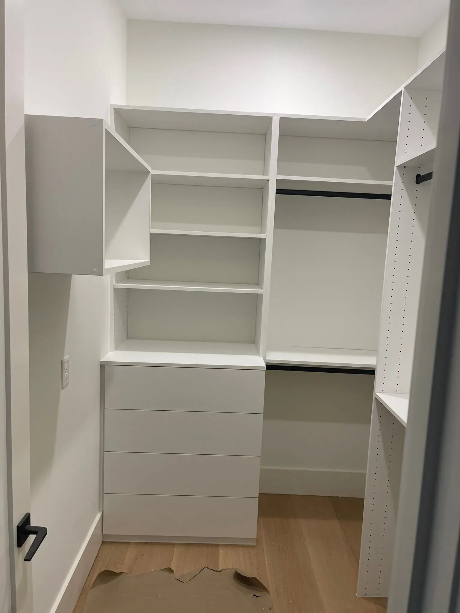 Empty walk-in closet with white built-in shelves and drawers, light wood floor, and gray walls.