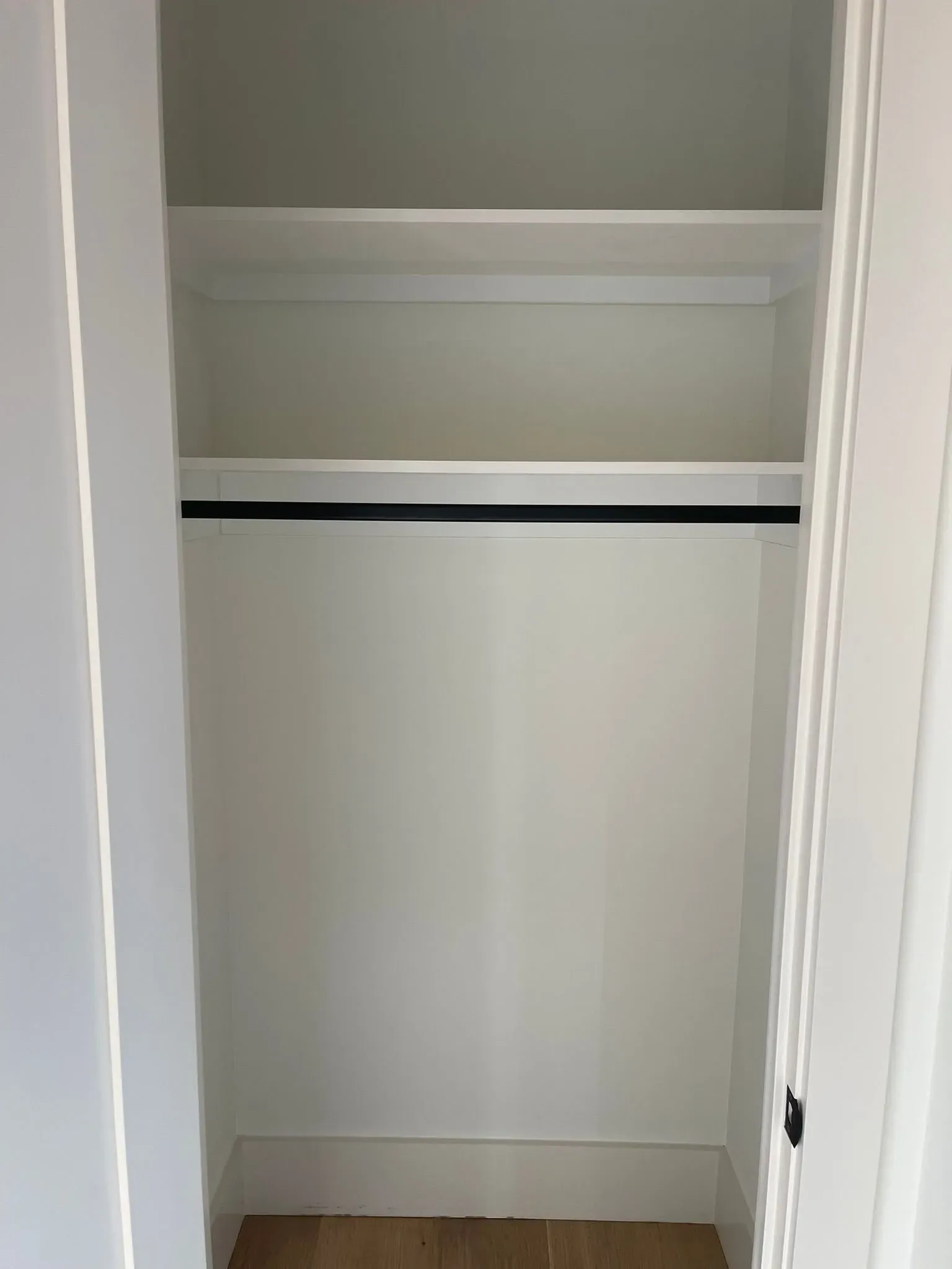 Empty white closet with a top shelf and hanging rod, viewed with the door open.