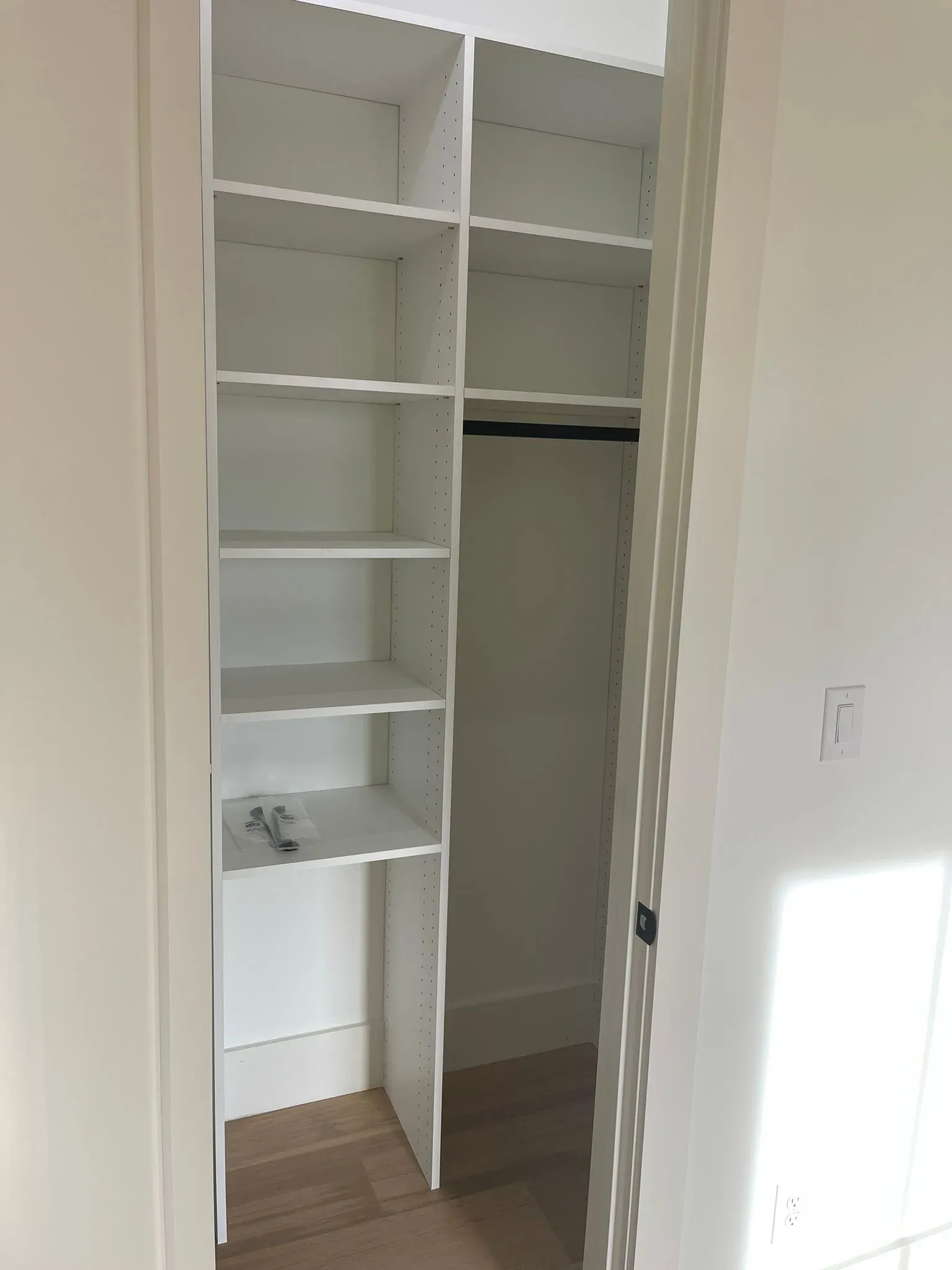 Open closet with white shelves, hanging rod, and wood floor in a narrow room.