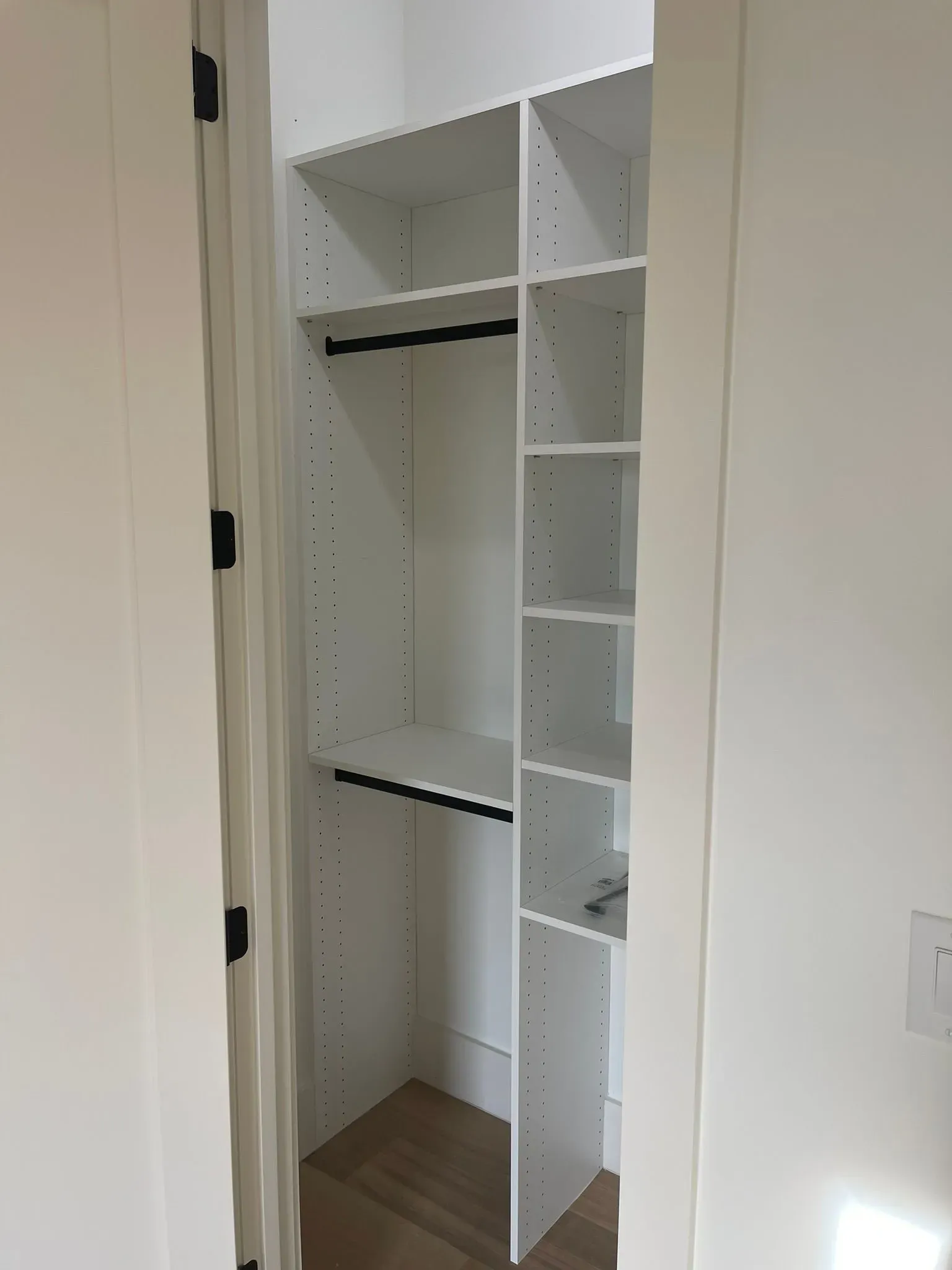 Open white closet with shelves and hanging rods, partially open door, empty interior.