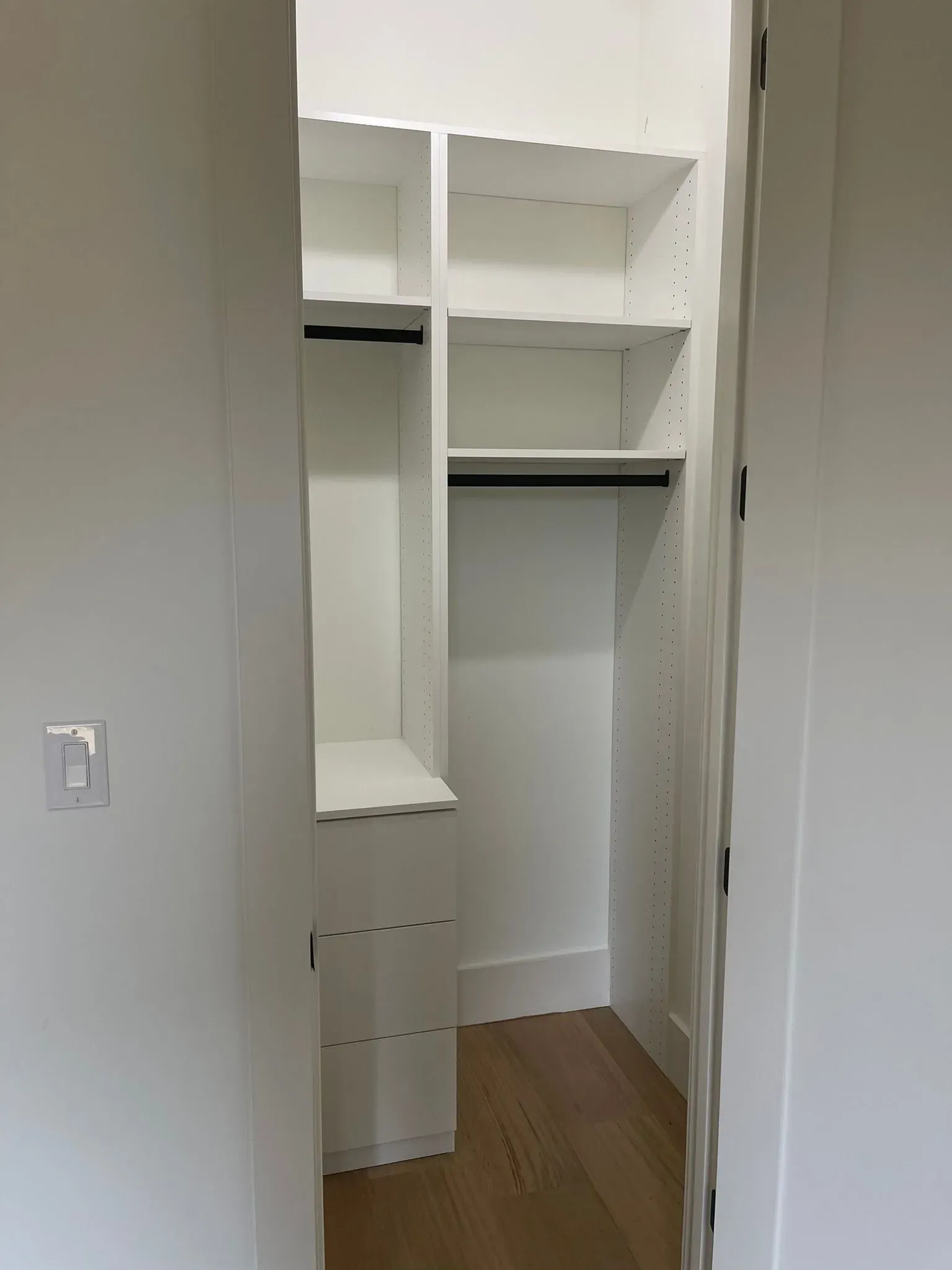 Open closet with white built-in shelves, hanging space, and drawers over a wood floor.