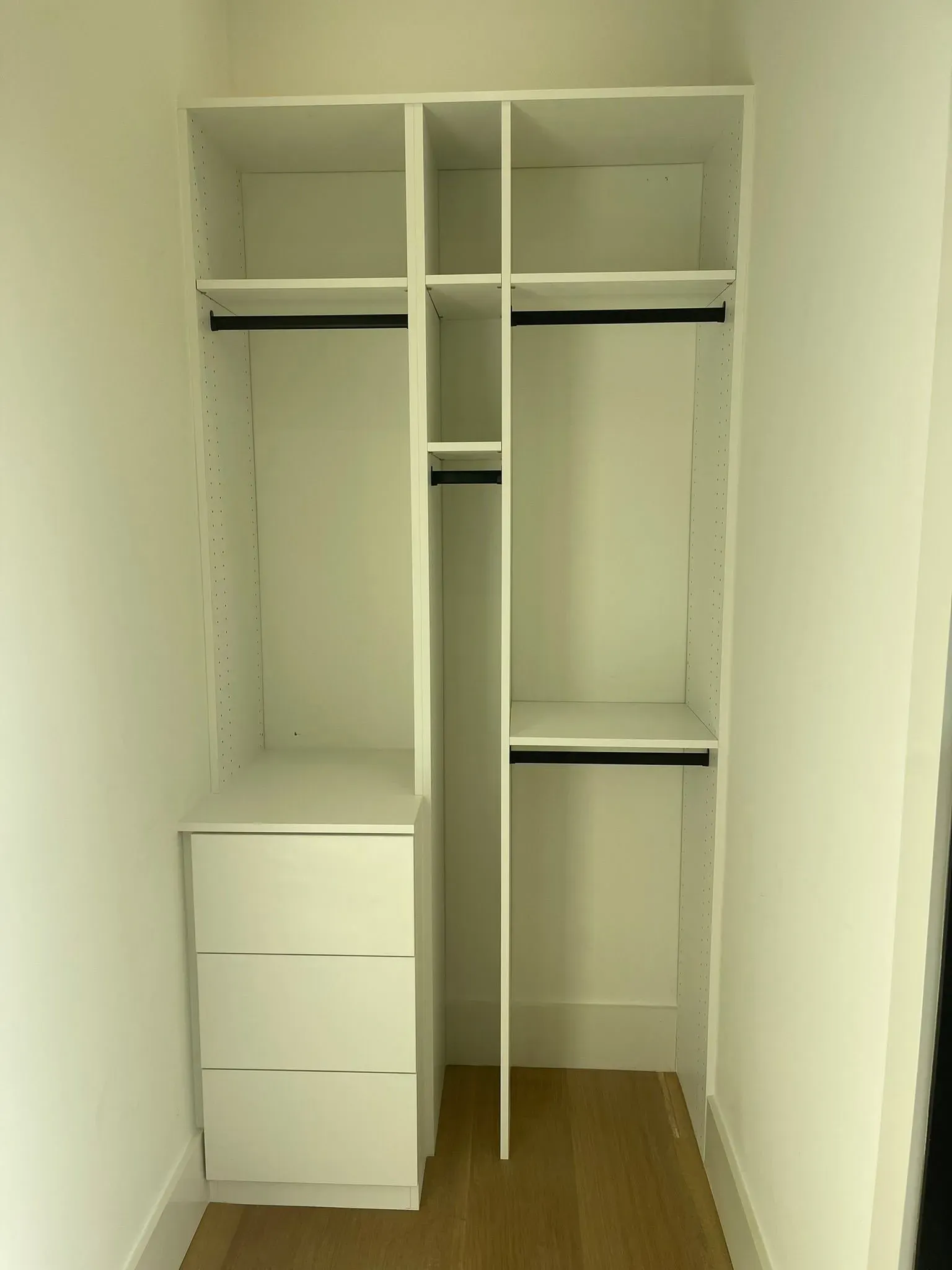 White walk-in closet with shelves, hanging rods, drawers, and a central divider.