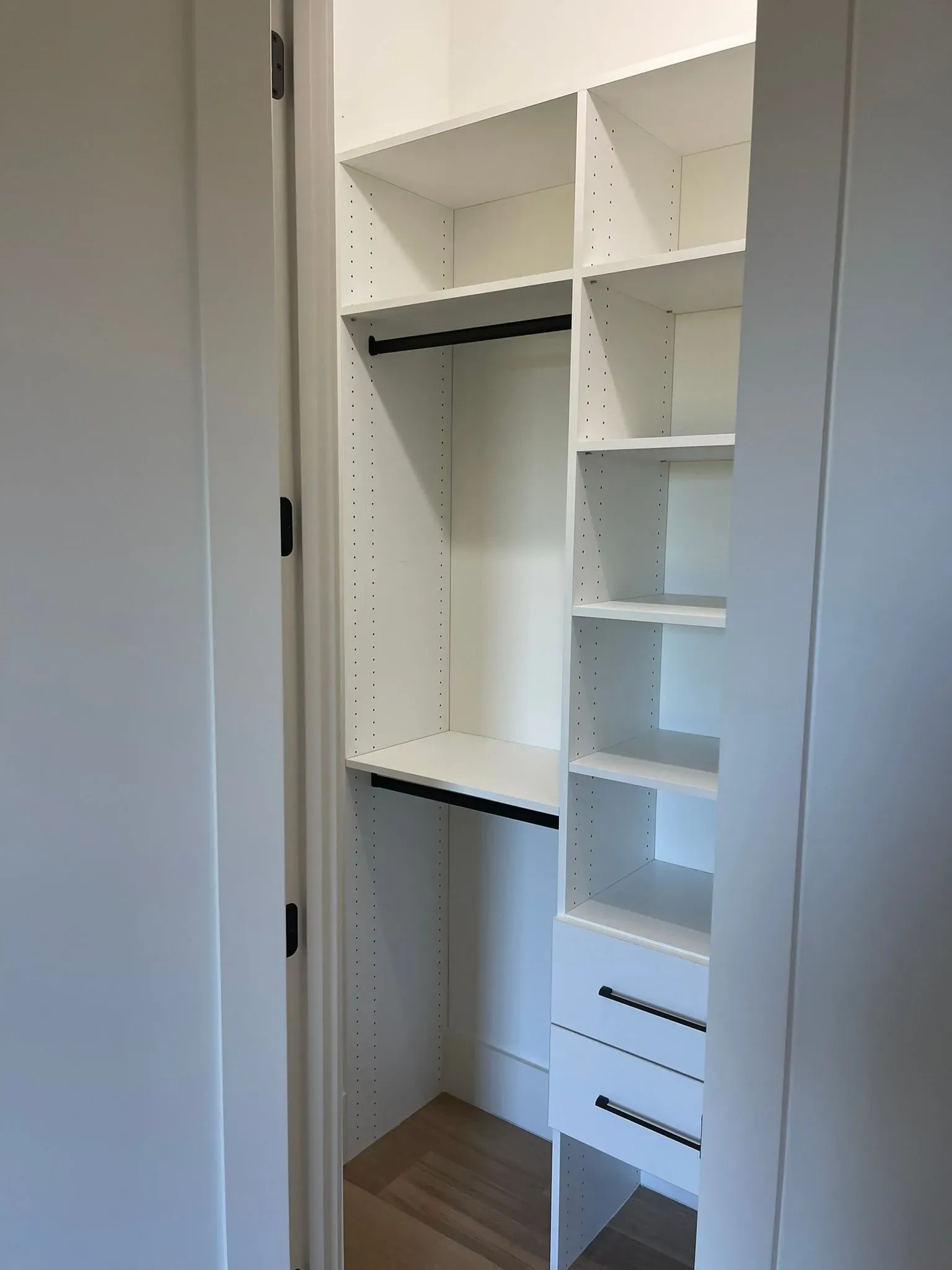 Open white closet with shelves, hanging rod, drawers, and wood floor.