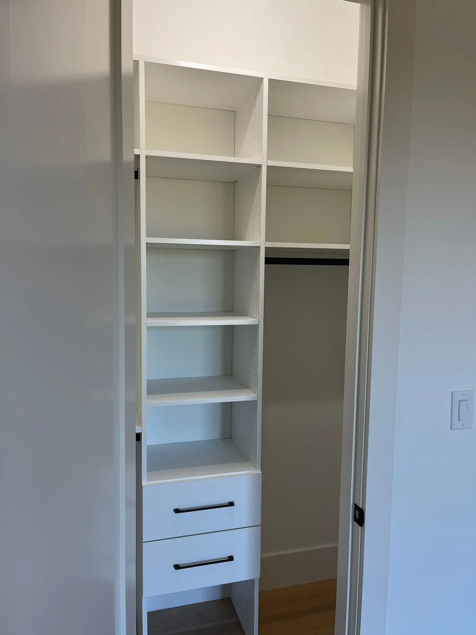 White built-in closet shelving with drawers and hanging space in a doorway.