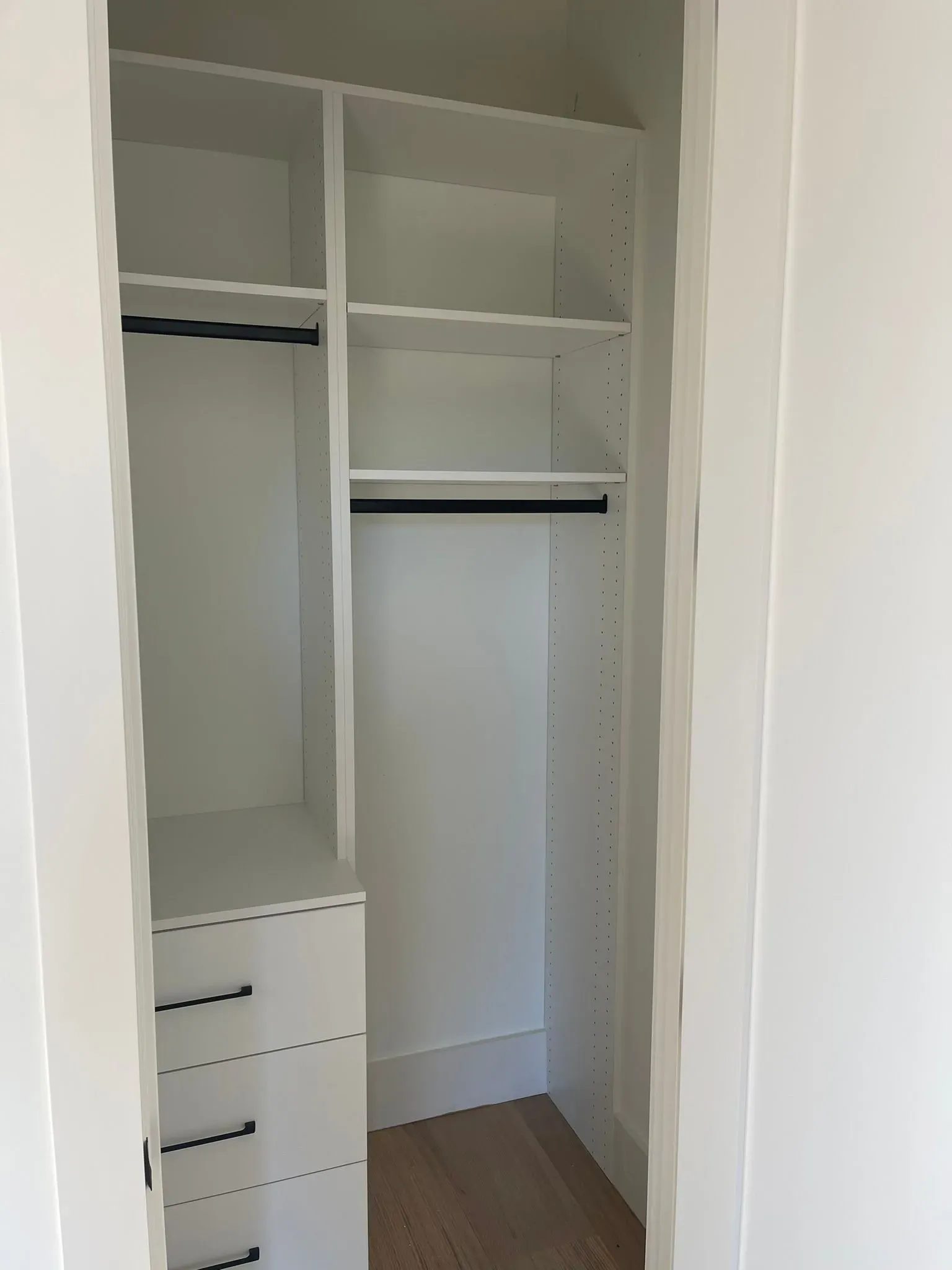 White built-in closet with shelves, hanging rods, and drawers in an empty room.