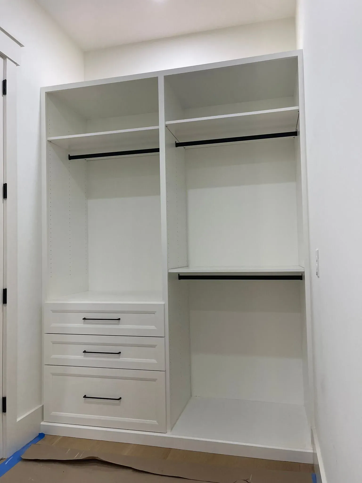 White open wardrobe in a bright room, with hanging rails and drawers on the left side.