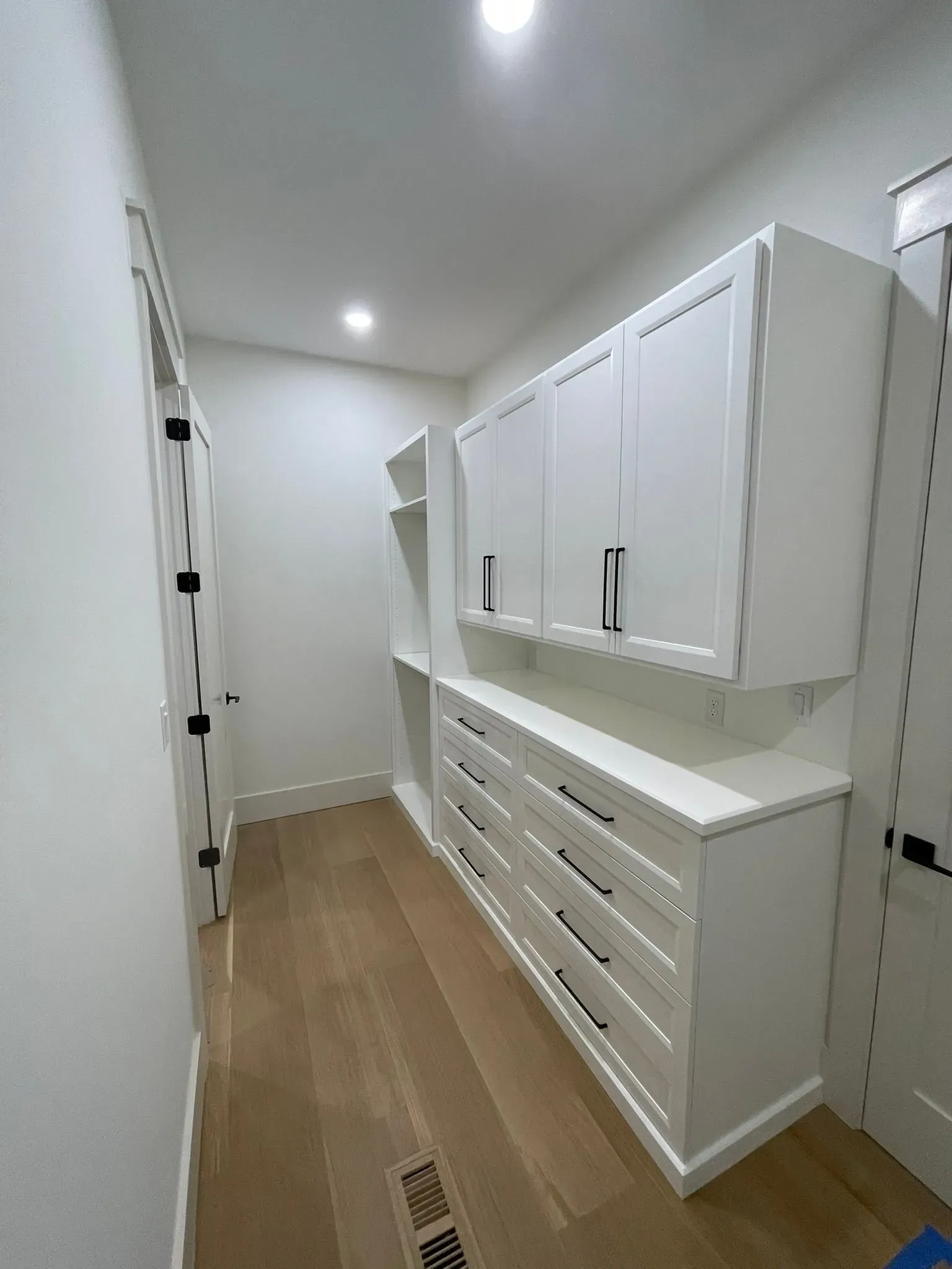 Bright narrow walk-in closet with white cabinets, drawers, and wood flooring