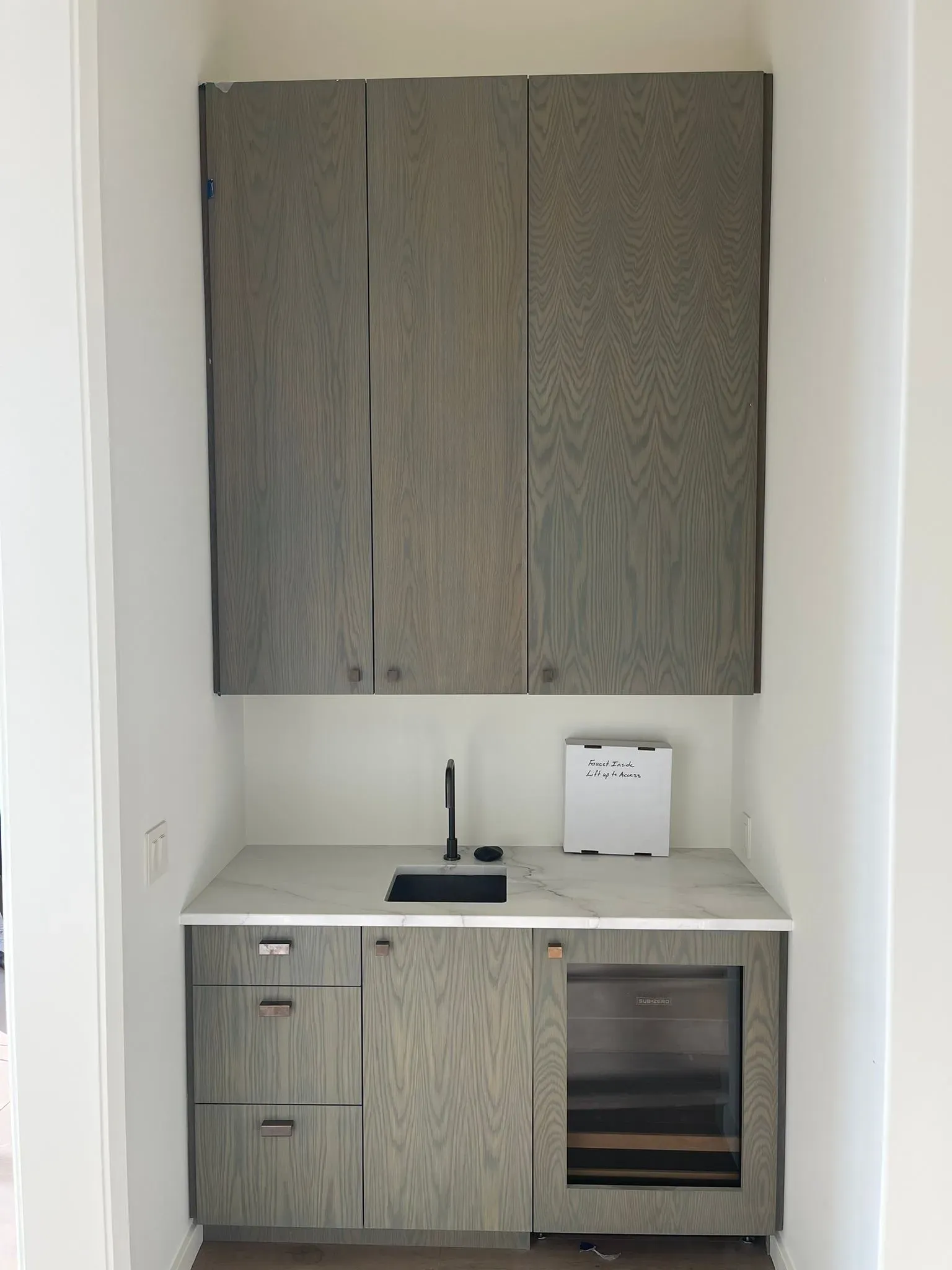 Modern kitchenette with gray cabinets, white countertop, black sink, and built-in wine cooler in a small alcove