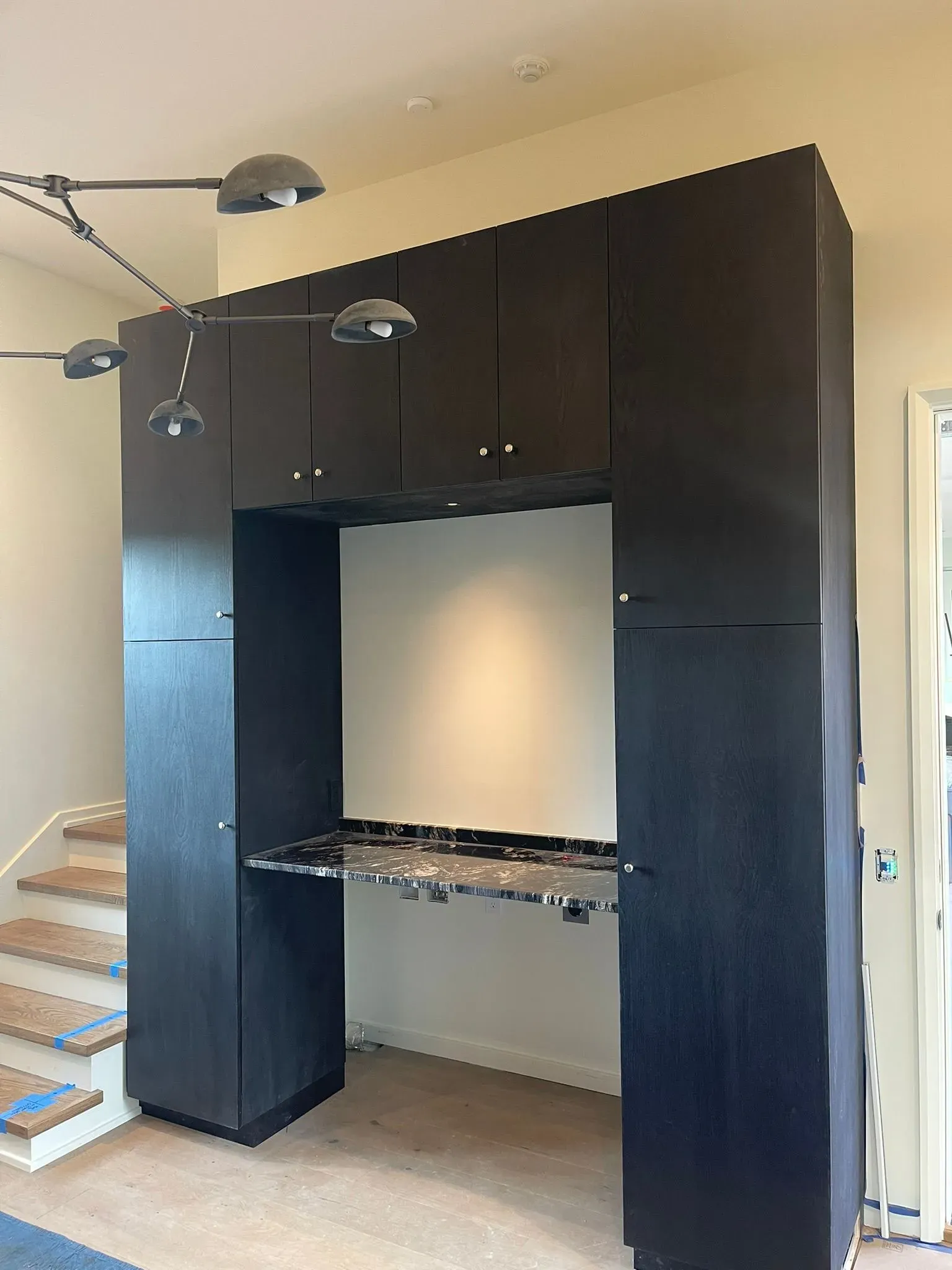 Built-in black cabinet framing a wall niche with a shelf and pendant lights in a room under construction