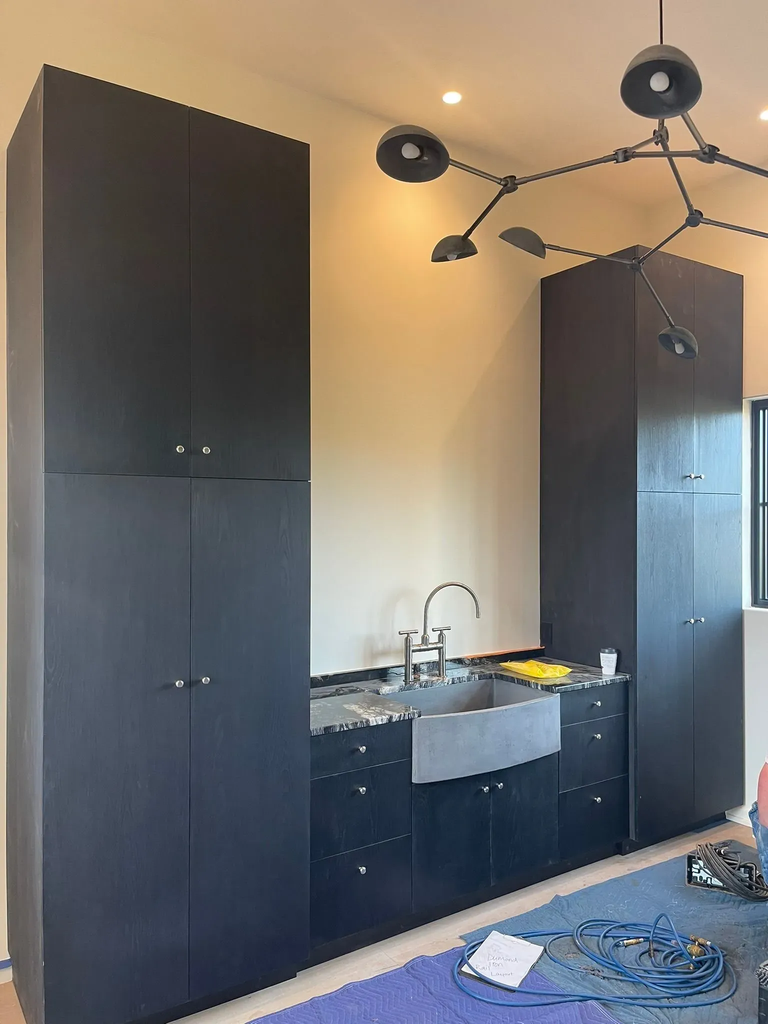 Modern kitchen with dark cabinets, black granite counters, sink, and blue rug under a chandelier.