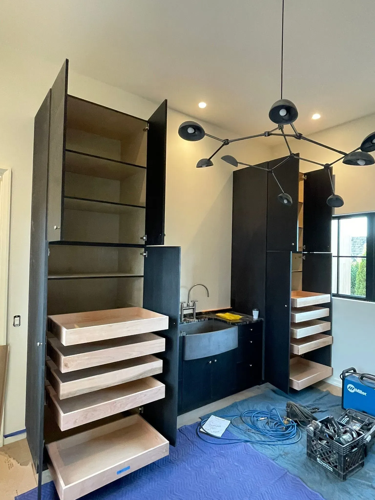 Modern closet room with open shelving, drawers, a black vanity, chandelier, and a blue rug on the floor