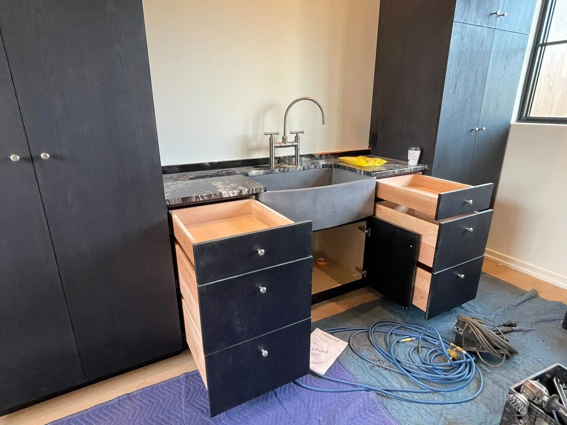 Unfinished kitchen cabinets and sink in a room, with tools and cables on the floor.