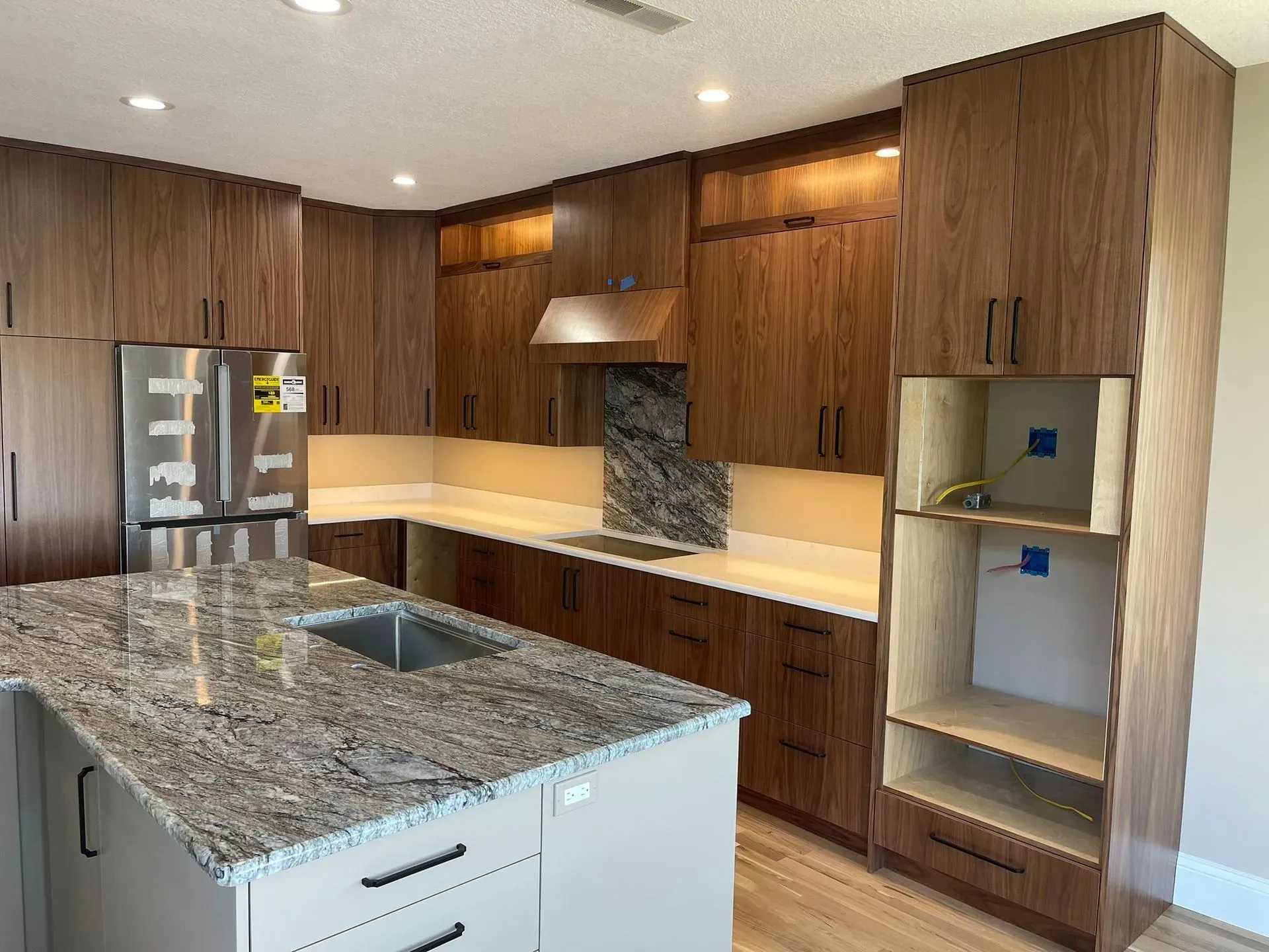 Modern kitchen with wood cabinets, granite island, stainless fridge, and built-in shelving niches