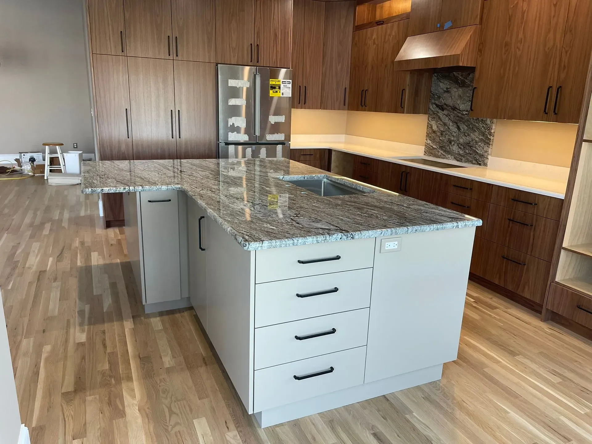 Modern kitchen with a large granite island, wood cabinets, stainless fridge, and hardwood floors