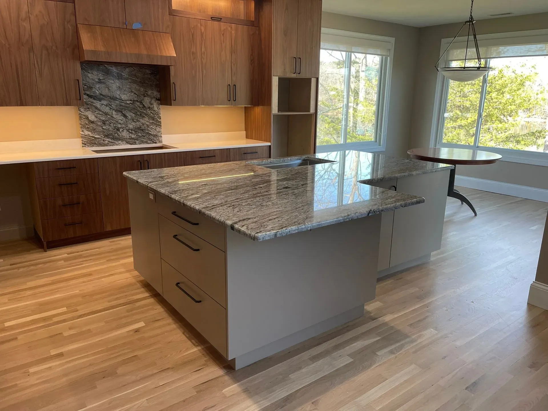 Modern kitchen with wood cabinets, granite island, and large windows overlooking greenery