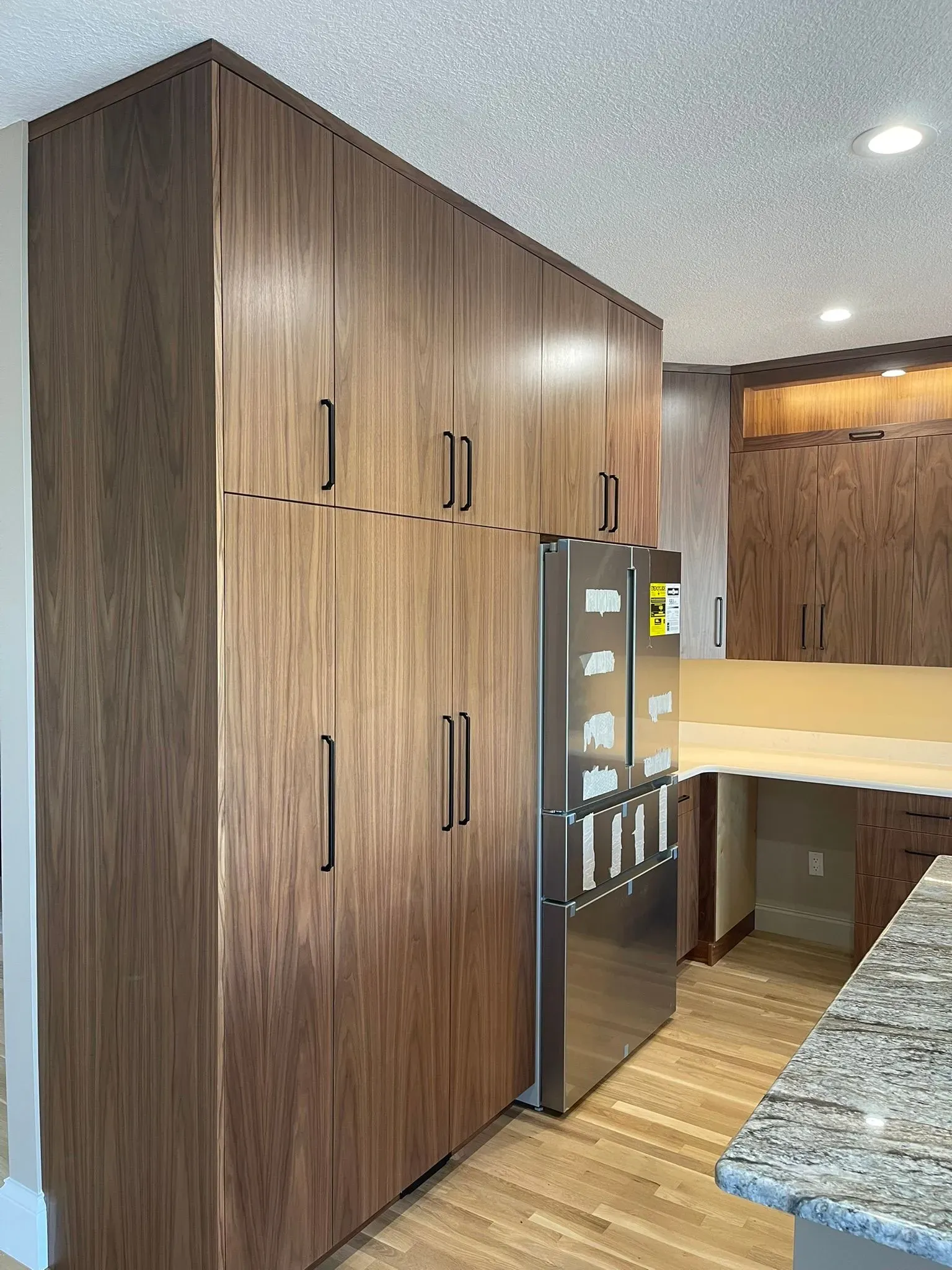Modern kitchen with tall wood cabinets, stainless fridge, and granite countertop with breakfast bar.