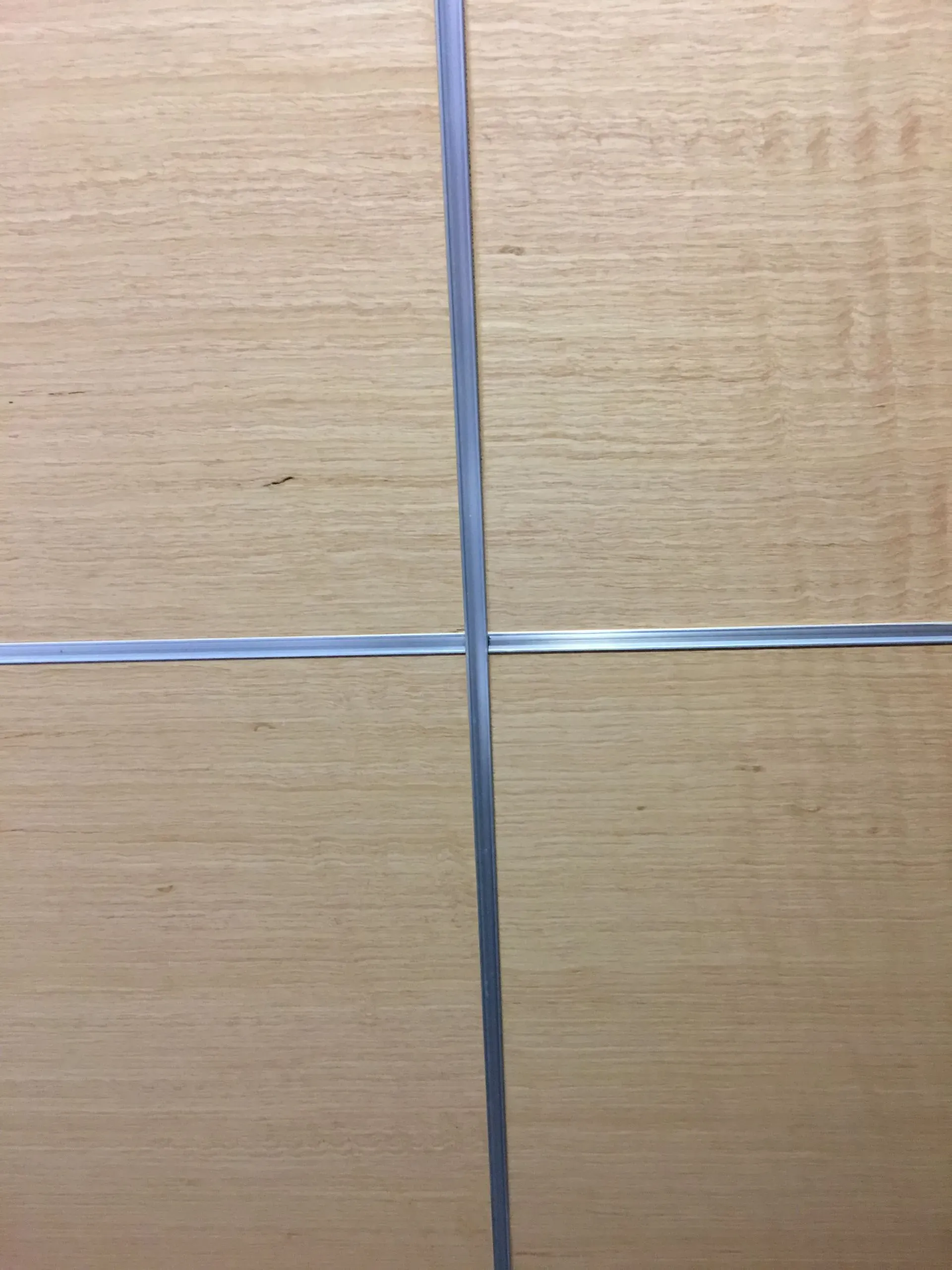 Close-up of light wood panels intersected by thin silver metal strips in a grid pattern