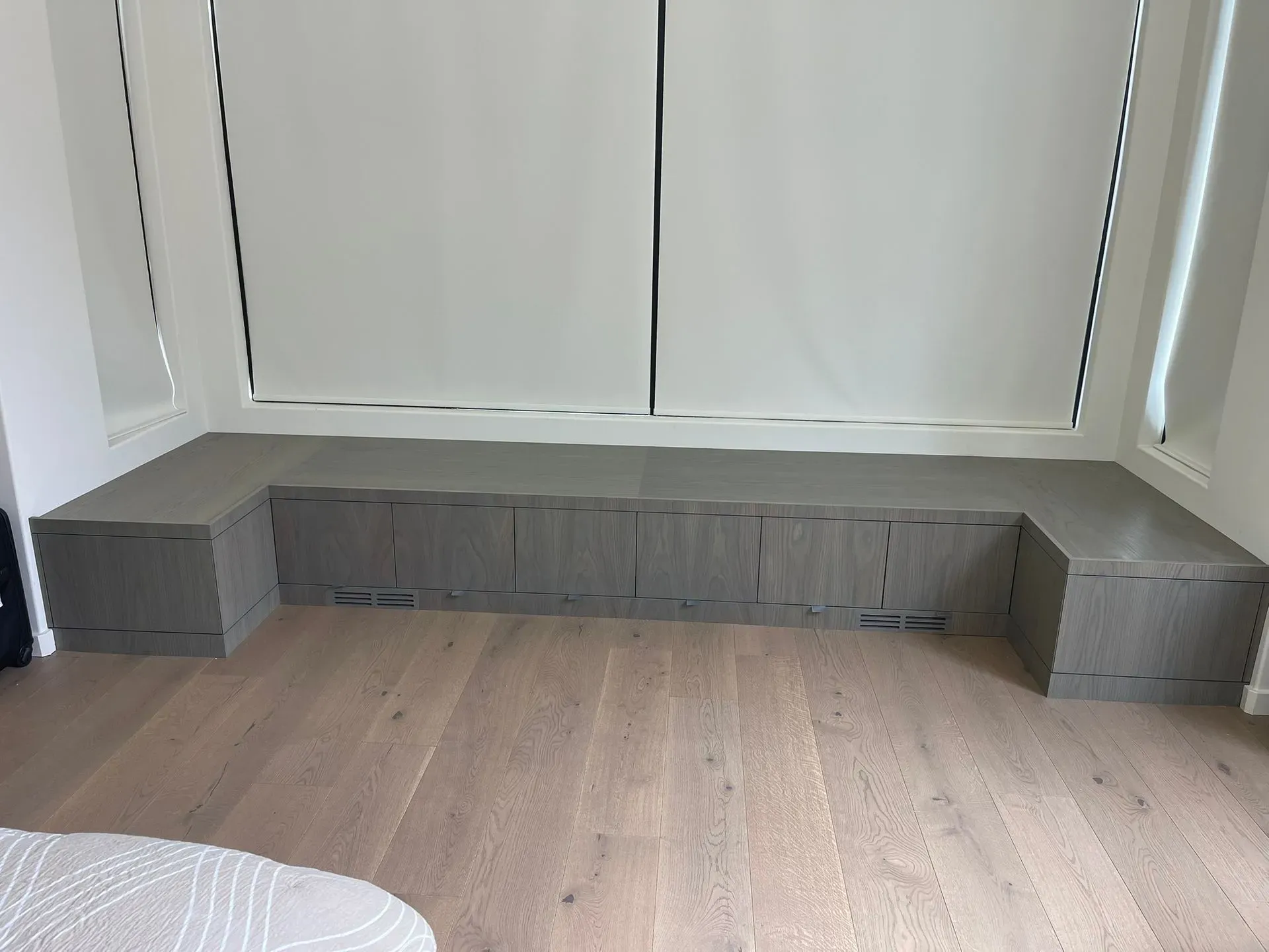 Built-in bench with gray cubbies against a wall in a light wood-floored room