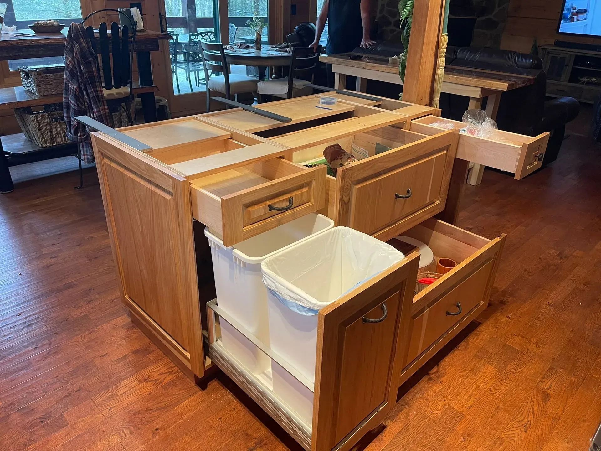 Wooden kitchen island with open drawers and white storage bins on a hardwood floor in a rustic room