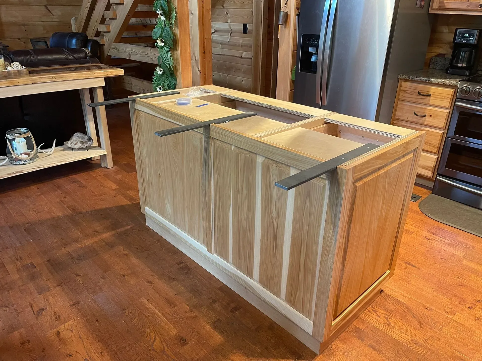 Wooden storage crate on a hardwood floor in a rustic room with shelving and a refrigerator in the background