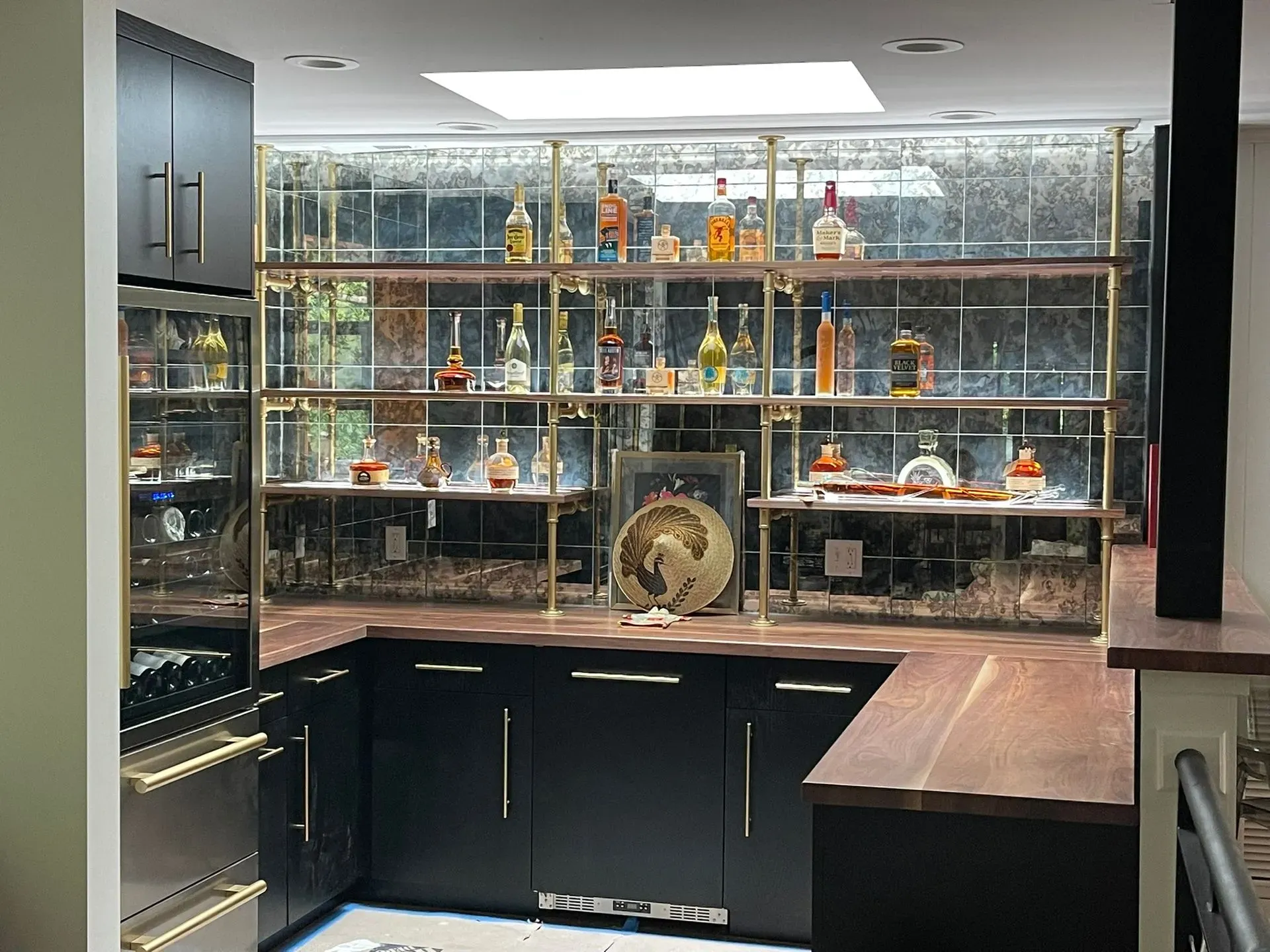 Modern home bar with glass shelves, liquor bottles, and dark cabinets beneath a bright display case