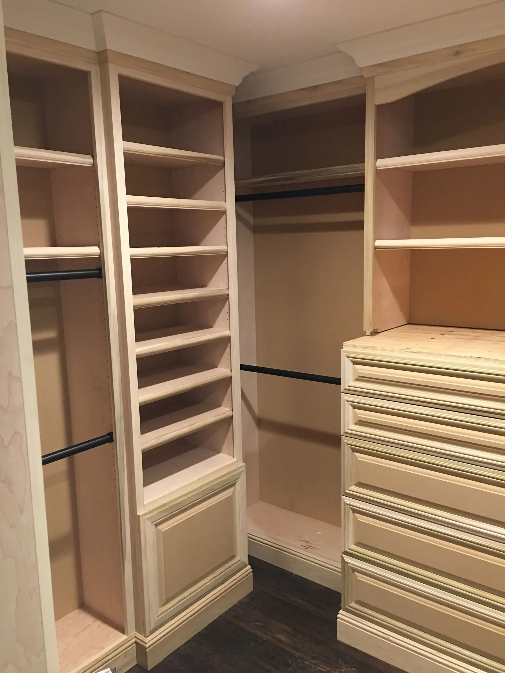 Walk-in closet with empty wooden shelves, hanging rods, and stacked white shoe shelves