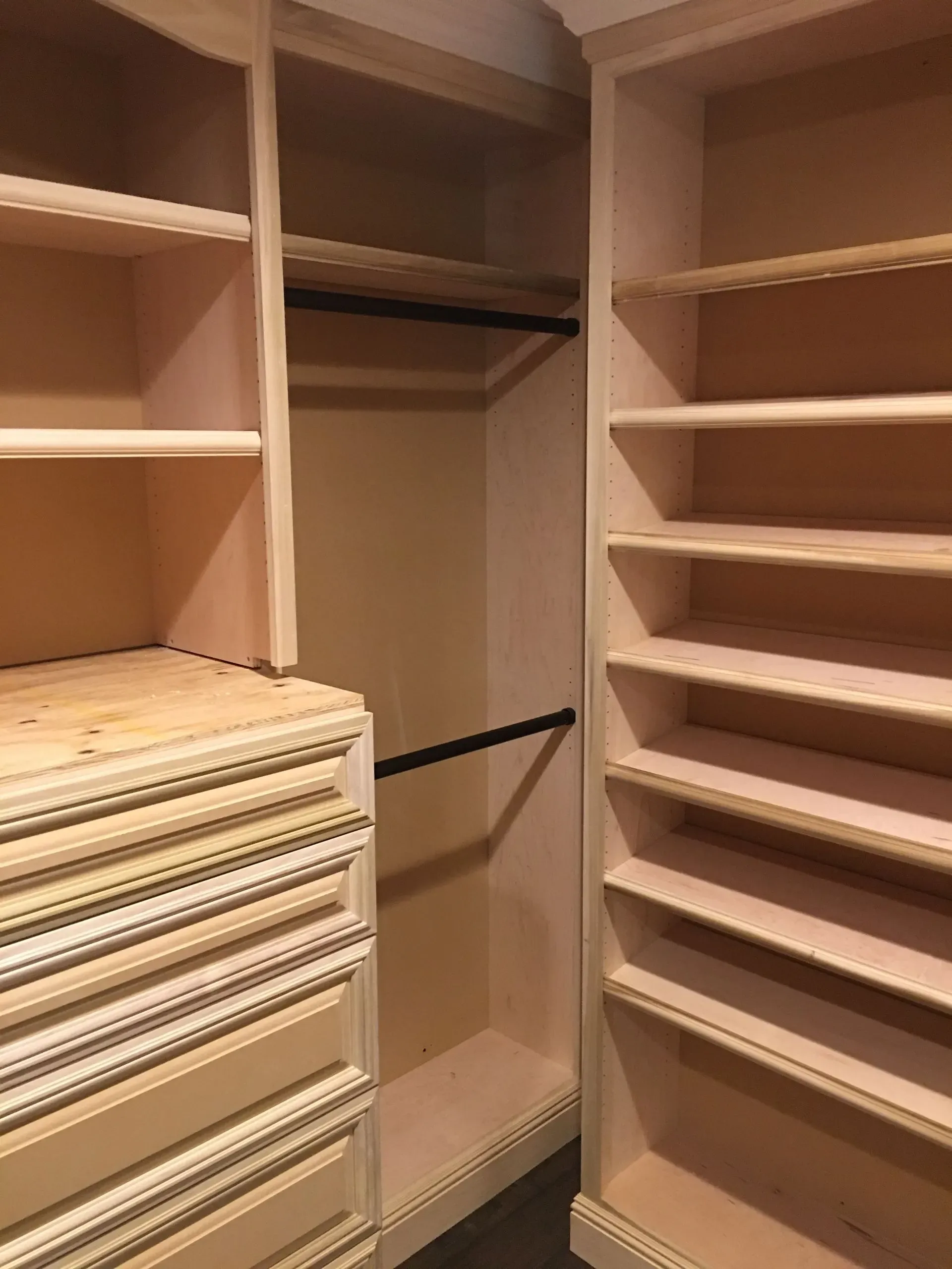 Walk-in closet with empty shelves and hanging rods beside a stack of folded clothes