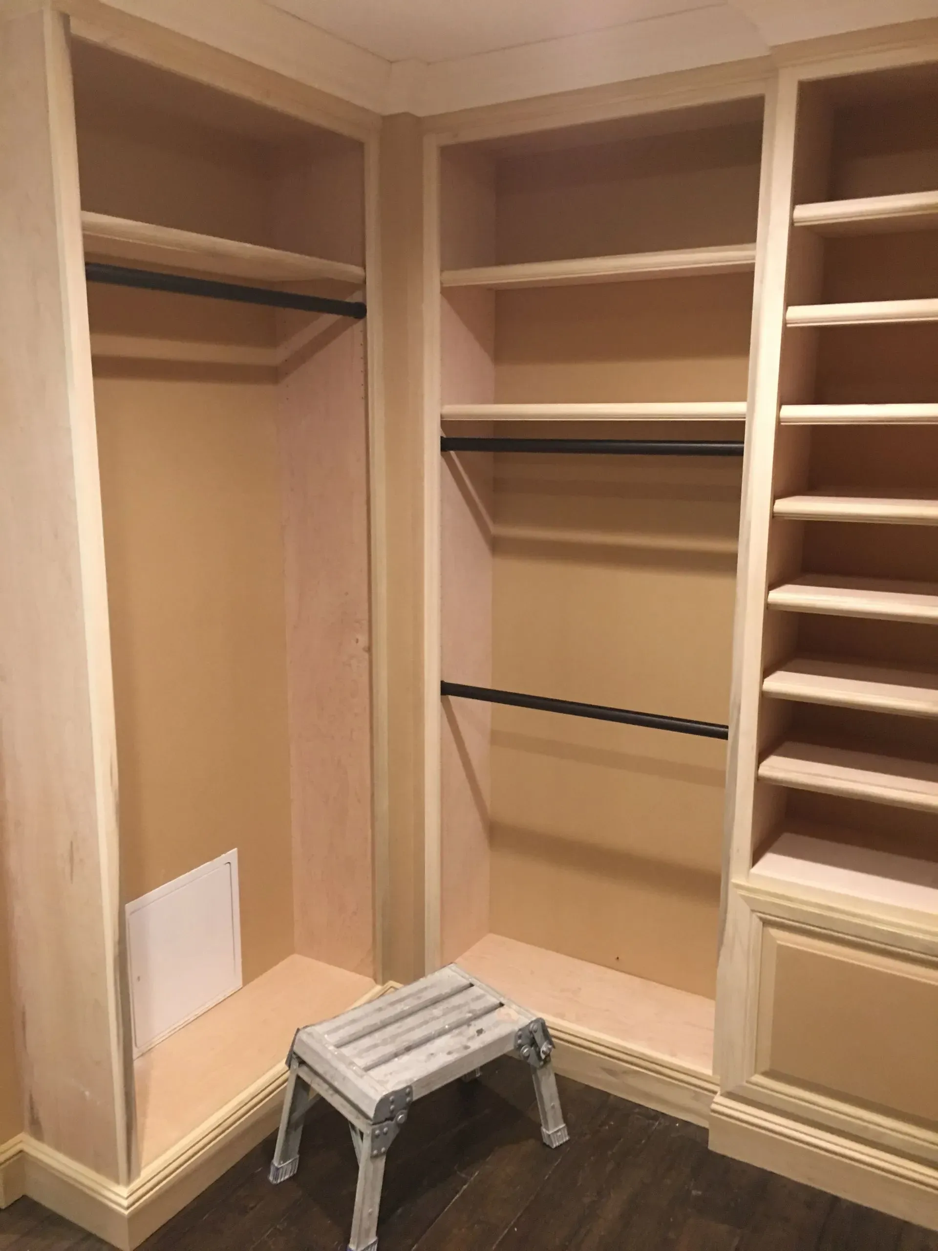 Empty beige walk-in closet with built-in shelves and a small step stool on the floor.
