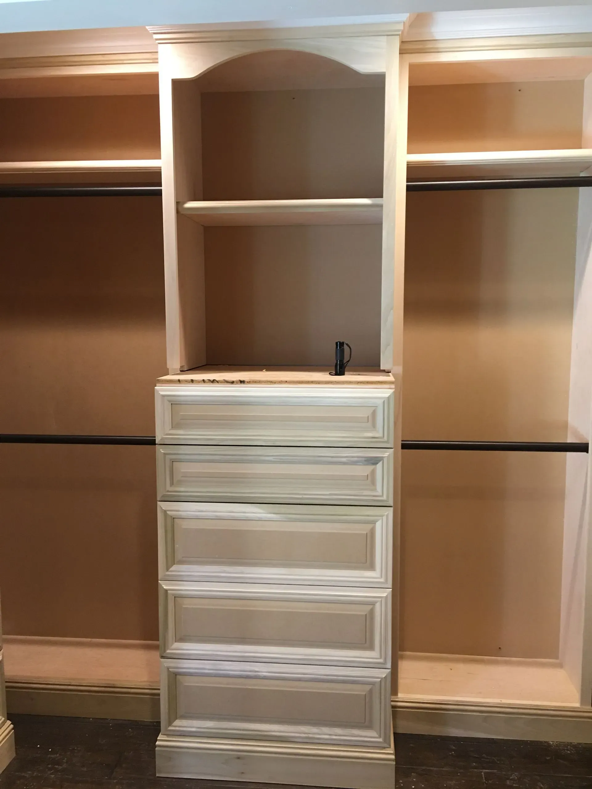 Built-in white closet organizer with drawers and shelves in a beige walk-in closet