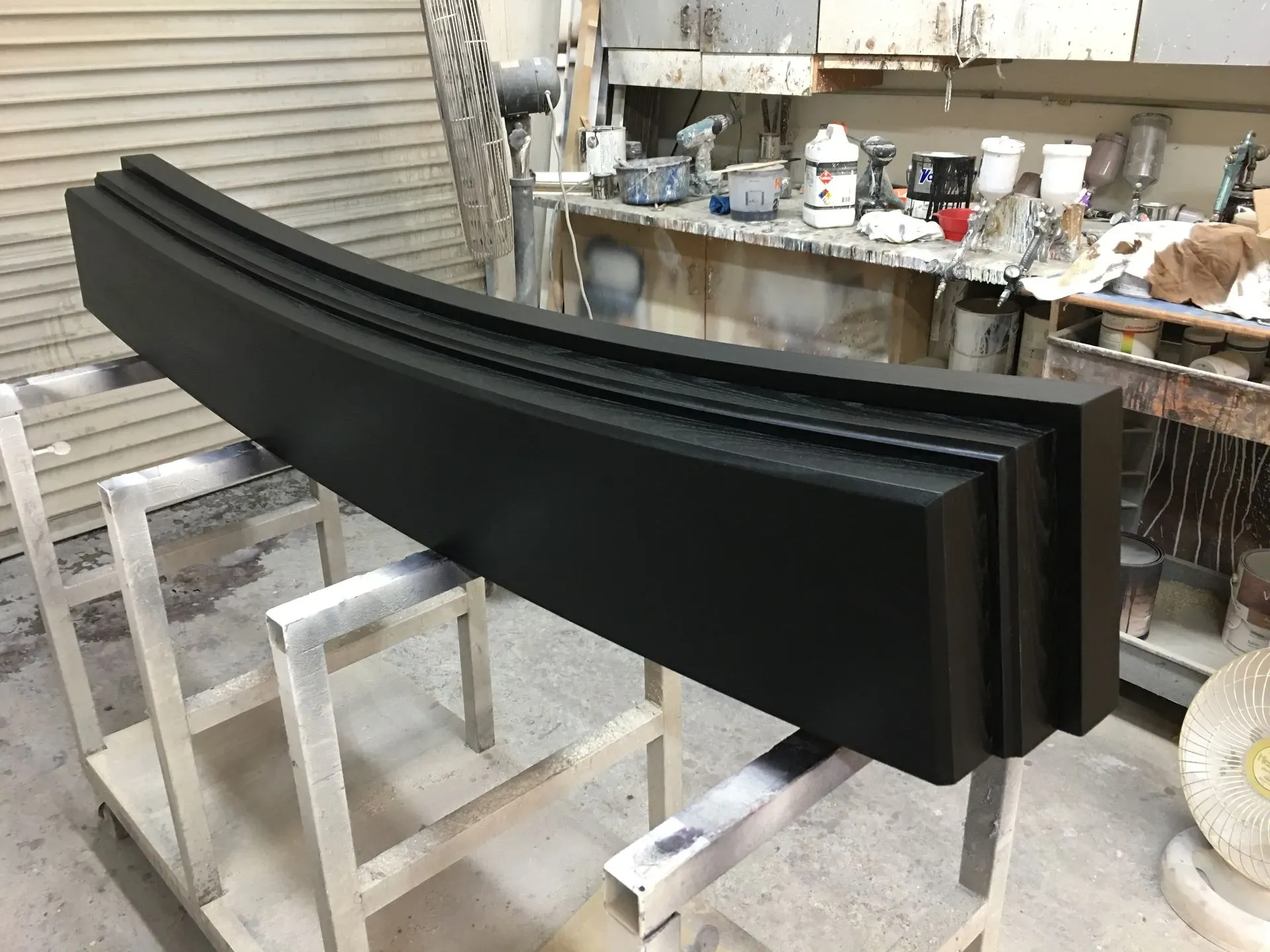Curved black painted panel leaning on a workbench in a workshop