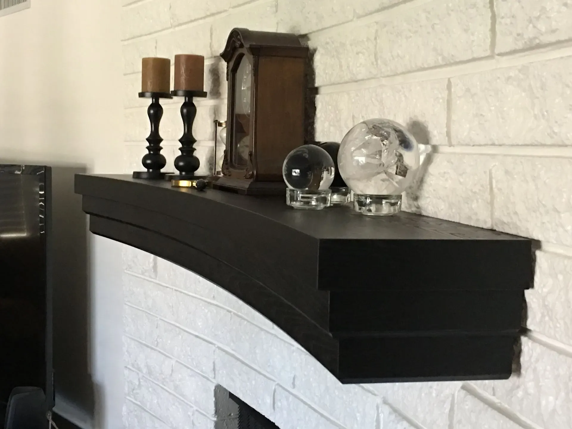 Black mantel shelf with candlesticks and glass decor on a white brick fireplace mantel