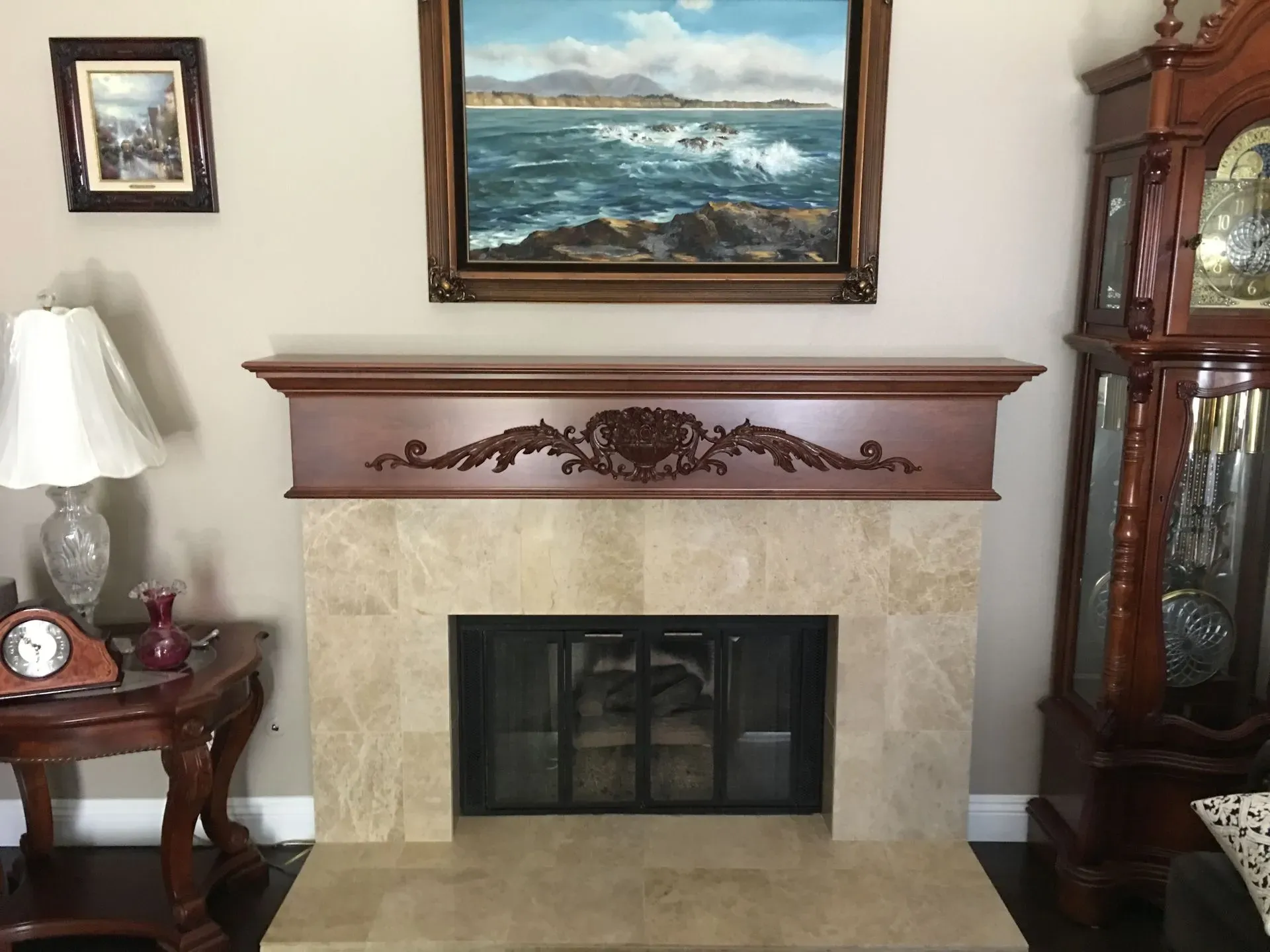 Living room fireplace with mantle, framed seascape, side table, lamp, and glass display cabinet