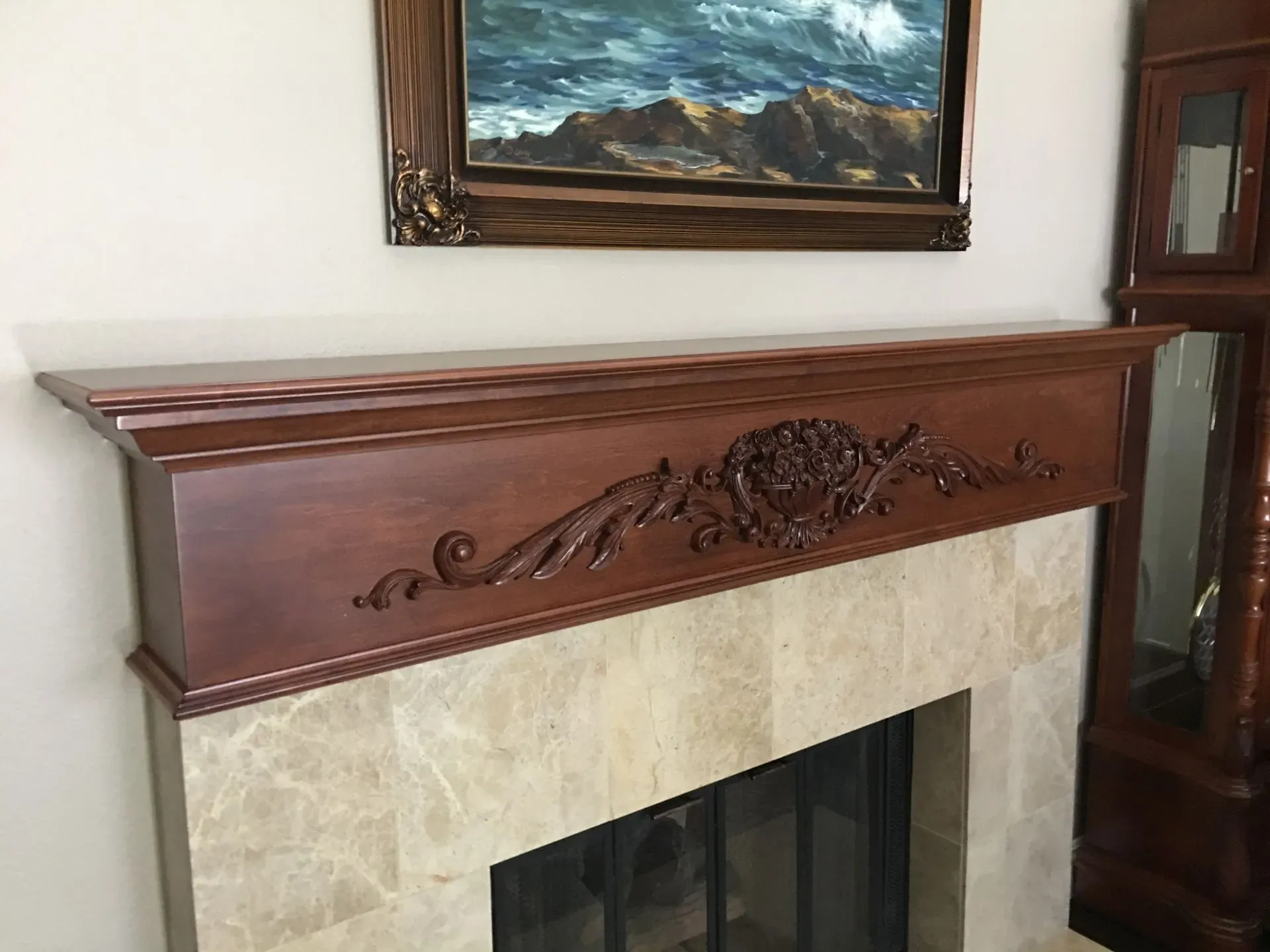 Ornate wooden fireplace mantel above a beige stone surround in a living room