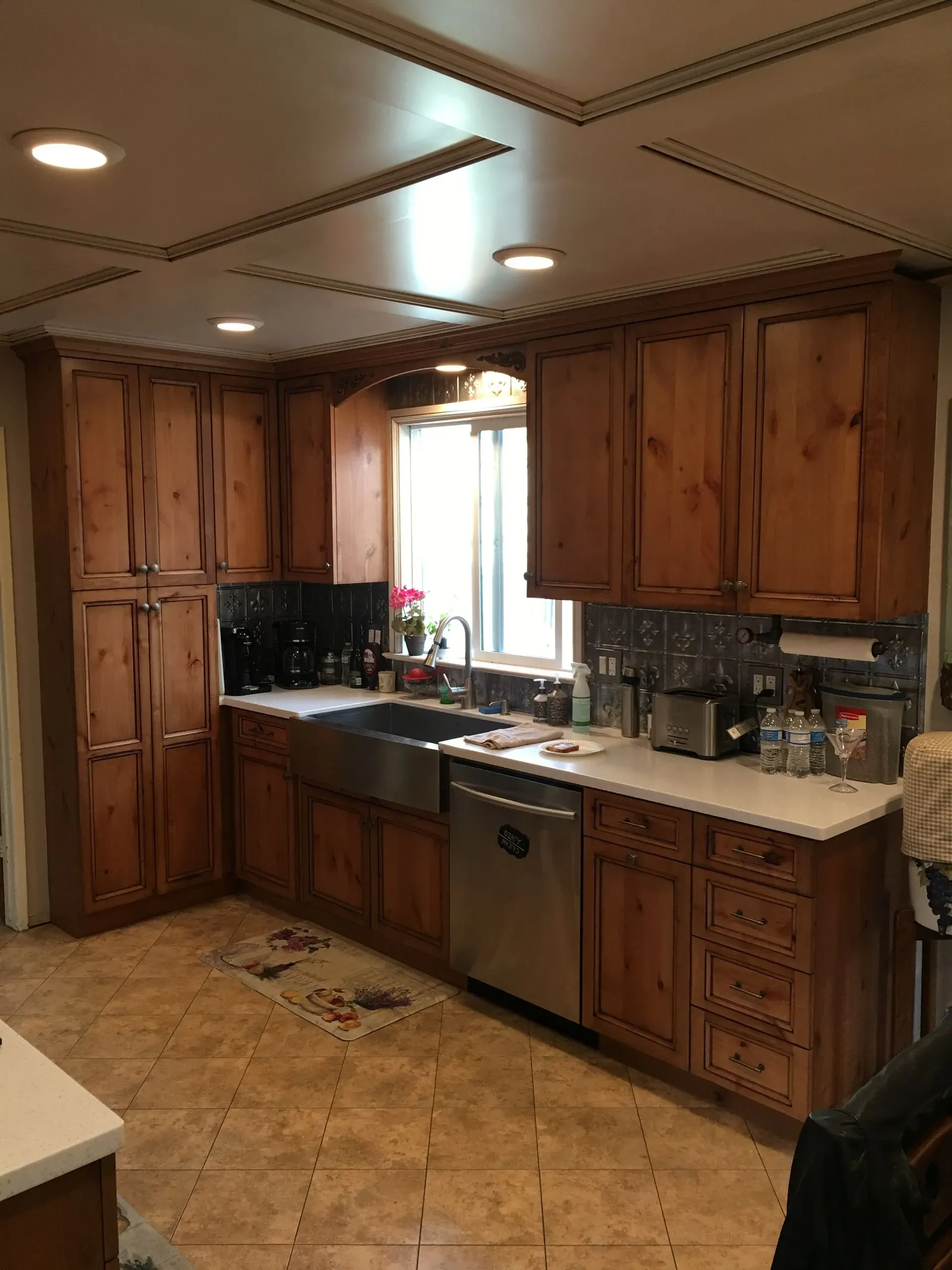Wooden kitchen with cabinets, stainless sink and dishwasher, tiled floor, and a window over the counter.
