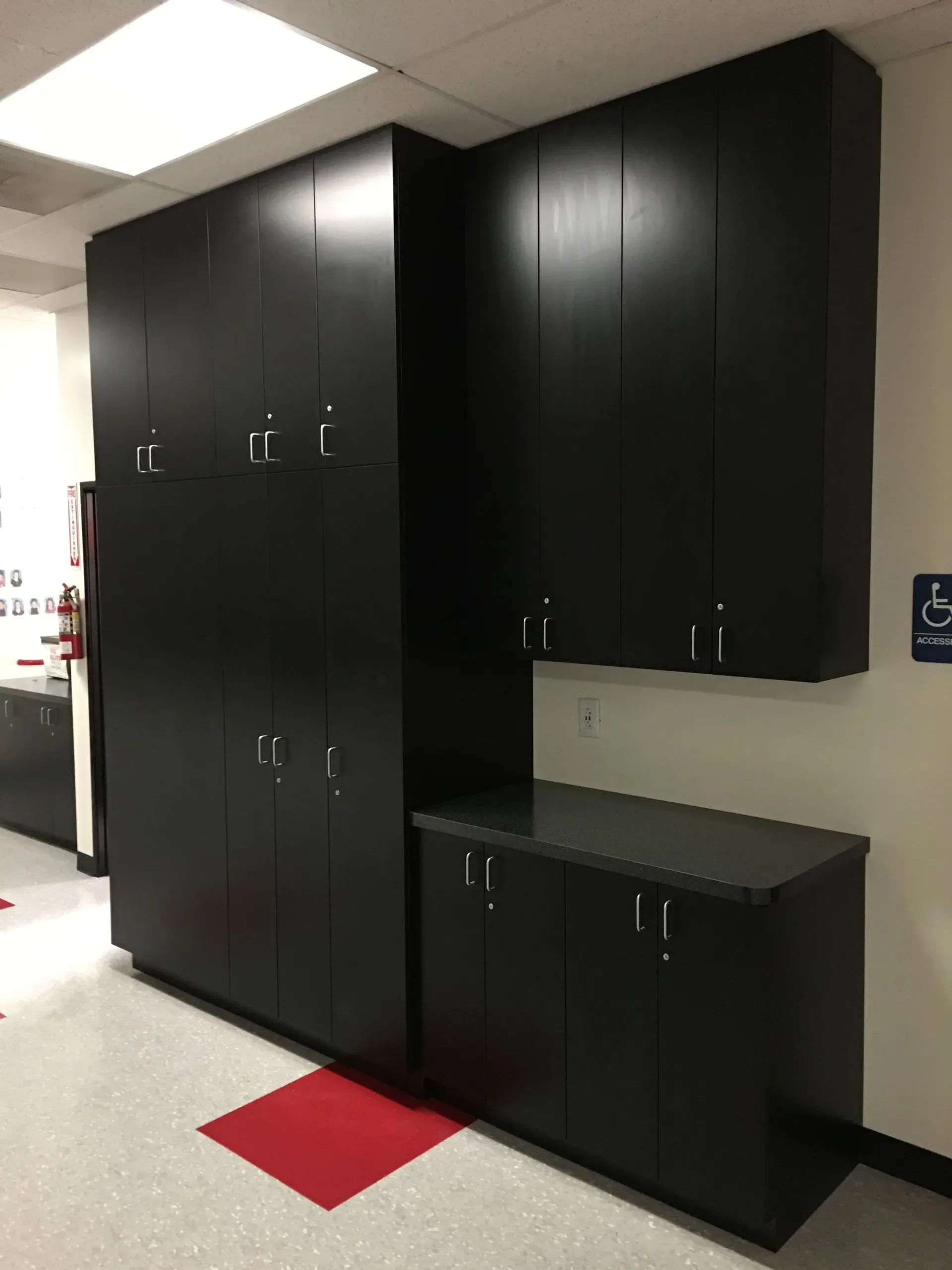 Black storage cabinets and a countertop in a bright hallway, with a red floor marker.