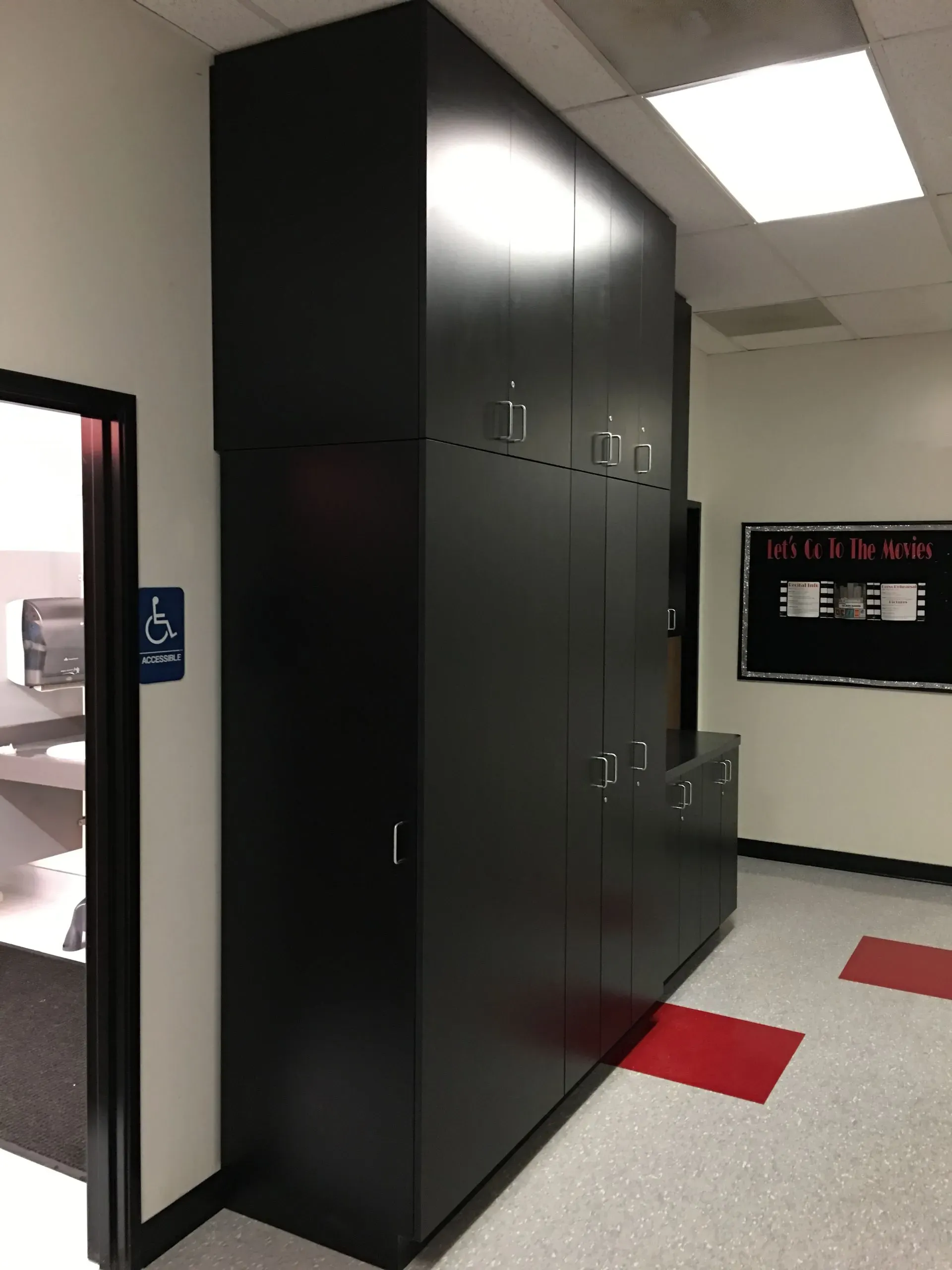 Black storage cabinets in a hallway with red-and-white tile flooring and overhead lights